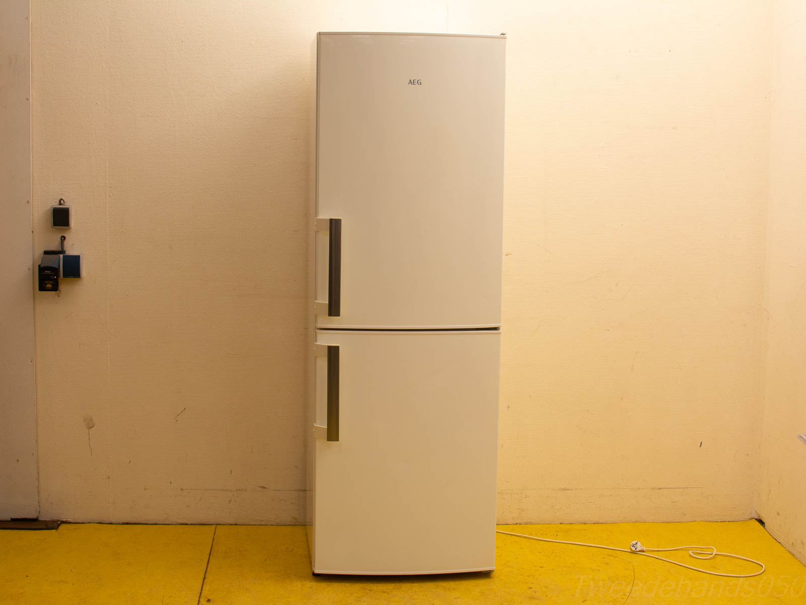 Modern AEG refrigerator against a light wall with yellow flooring and functional accessories.