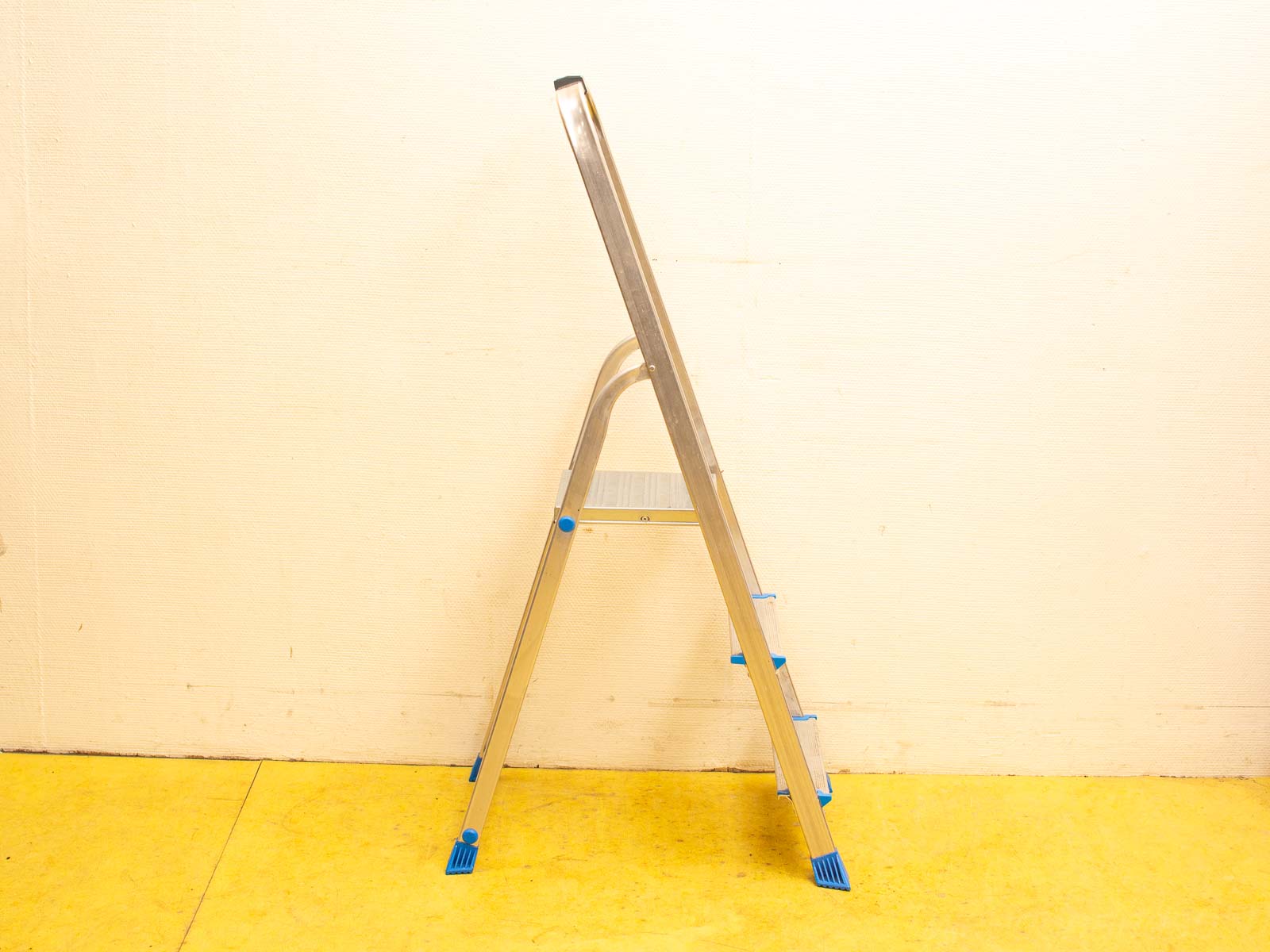 Sleek aluminum step ladder with blue rubber feet, ideal for safe use in any workspace.