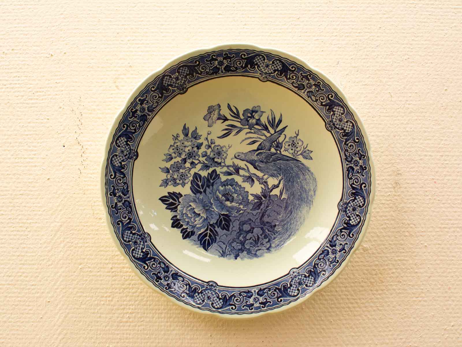 Elegant blue peacock ceramic plate with floral designs on a soft cream background.