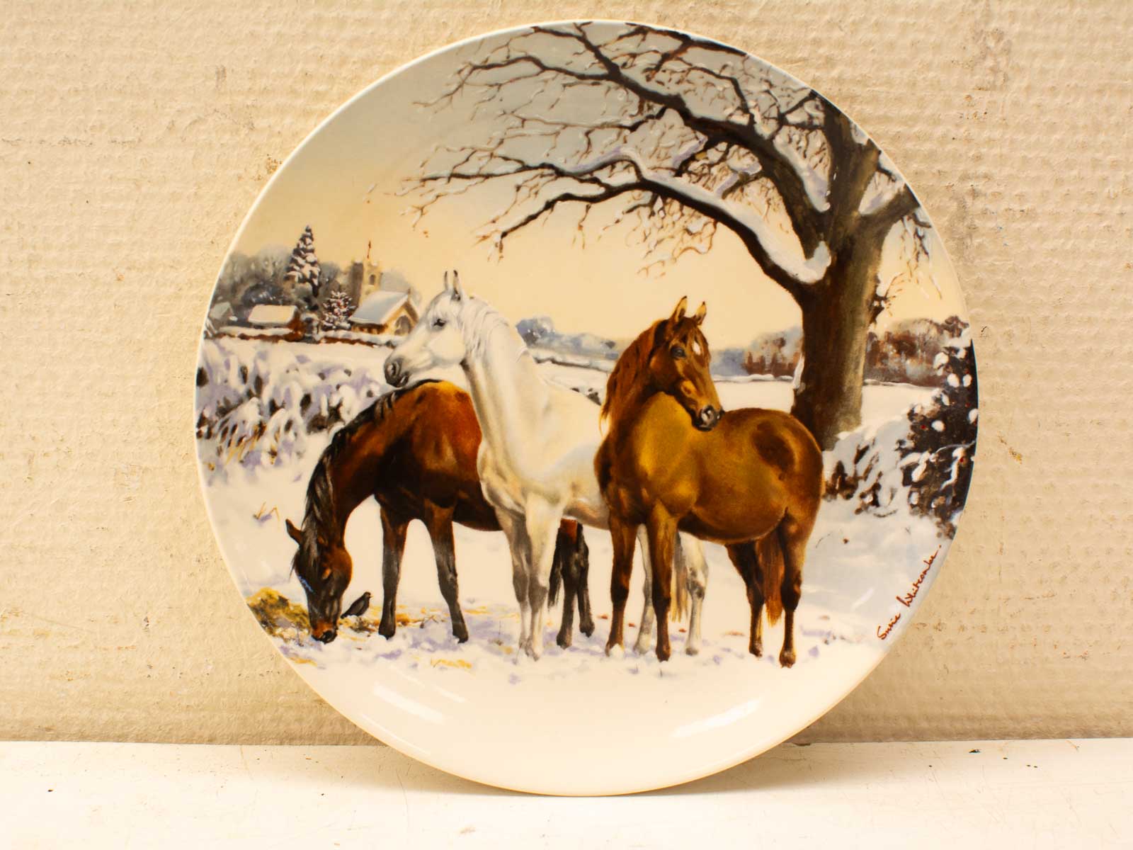 Serene winter scene with three horses on a decorative plate, showcasing equine beauty.