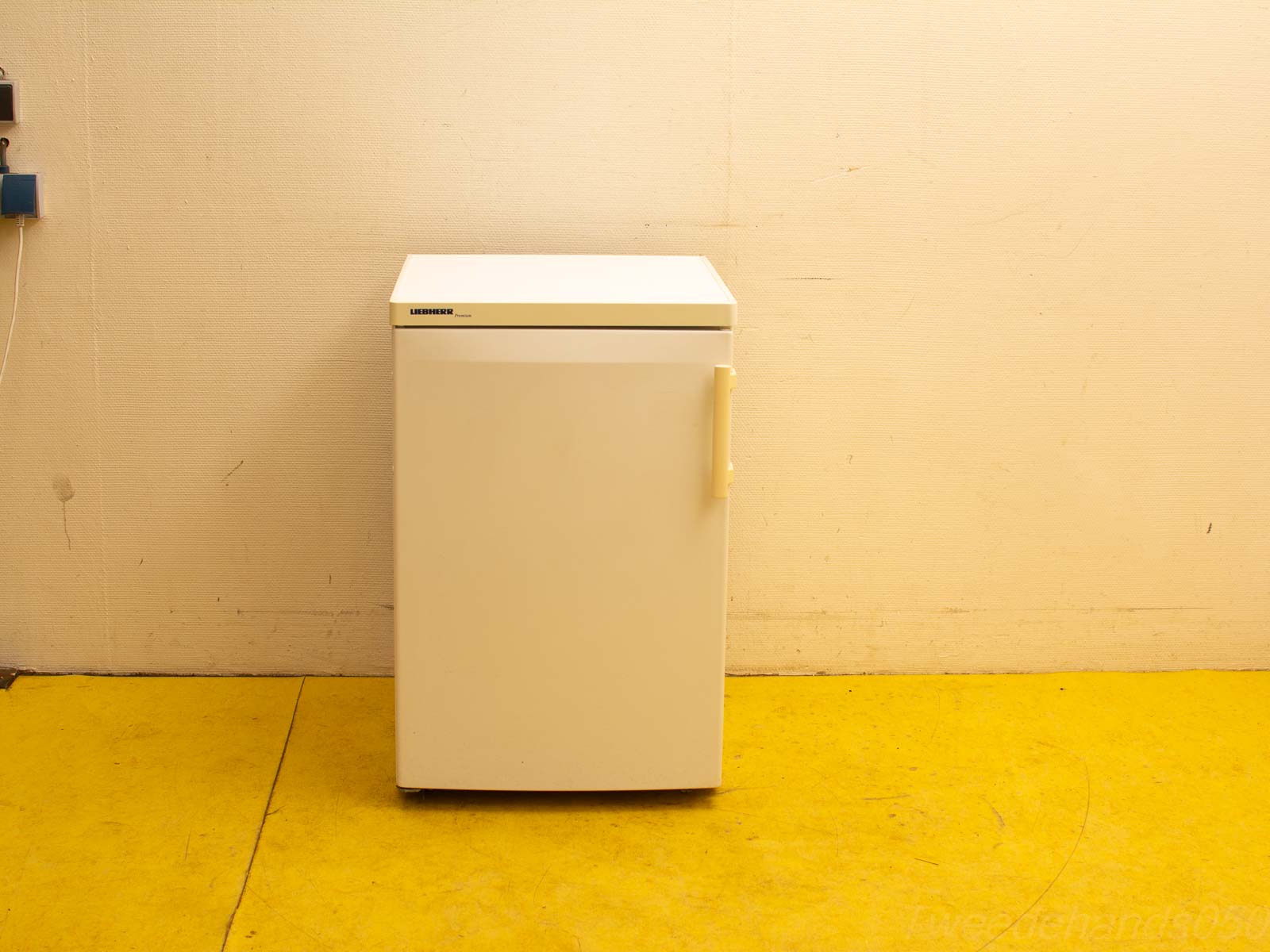 Compact white refrigerator with yellow handle, perfect for home or office spaces.