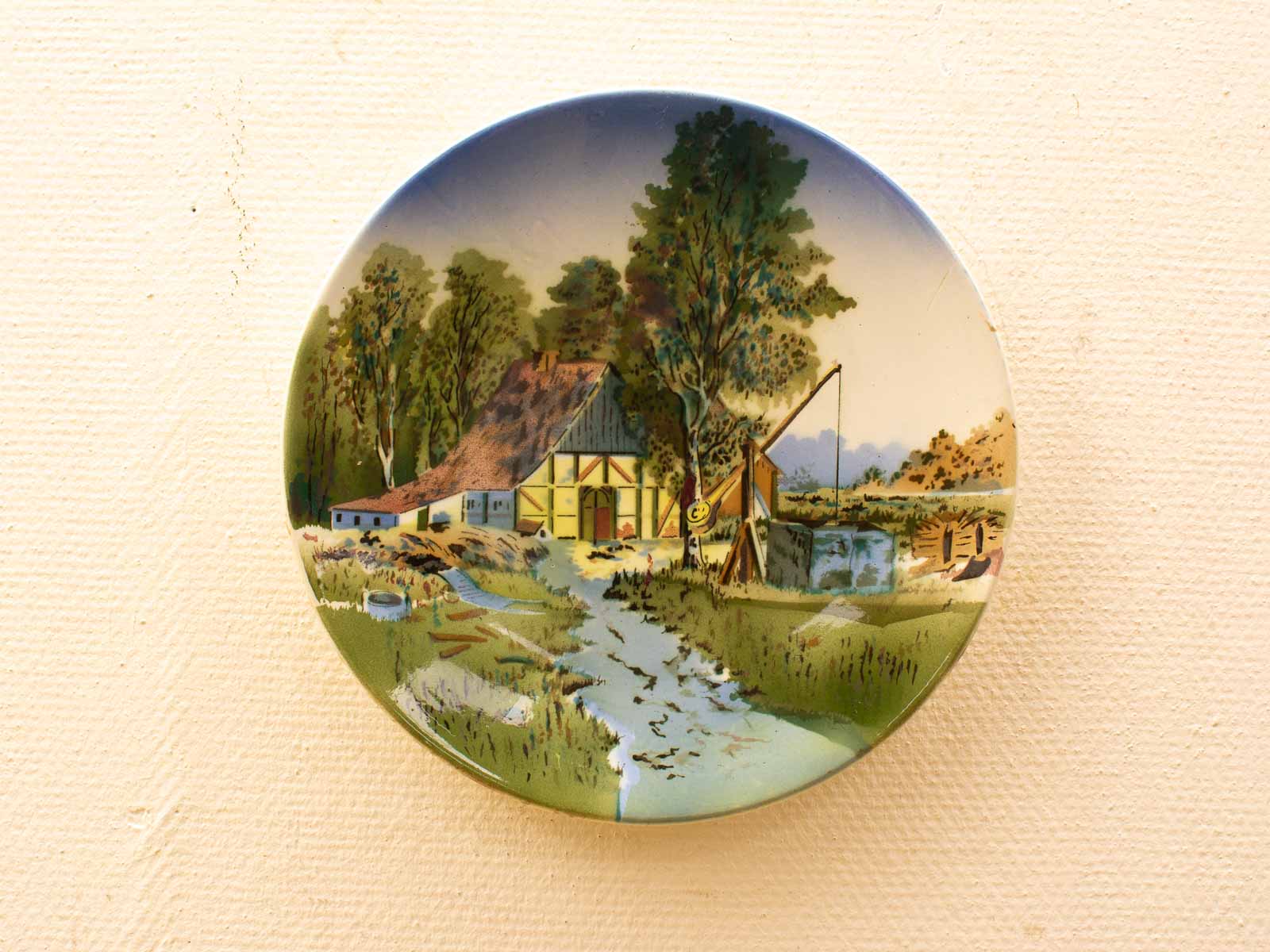 Charming decorative plate depicting a tranquil farmhouse and serene rural landscape scene.