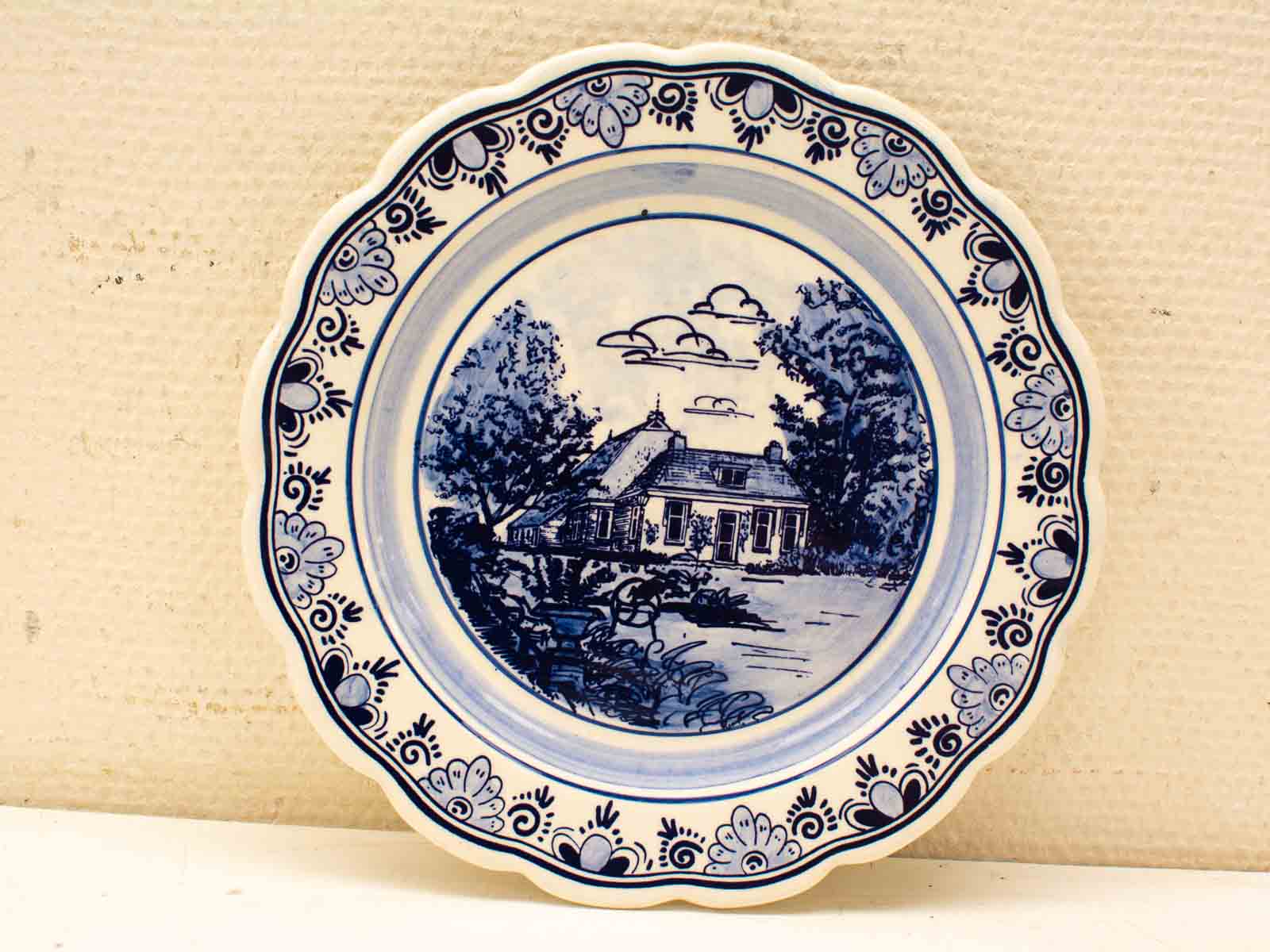 Charming blue and white plate featuring a cozy countryside house and elegant floral designs.