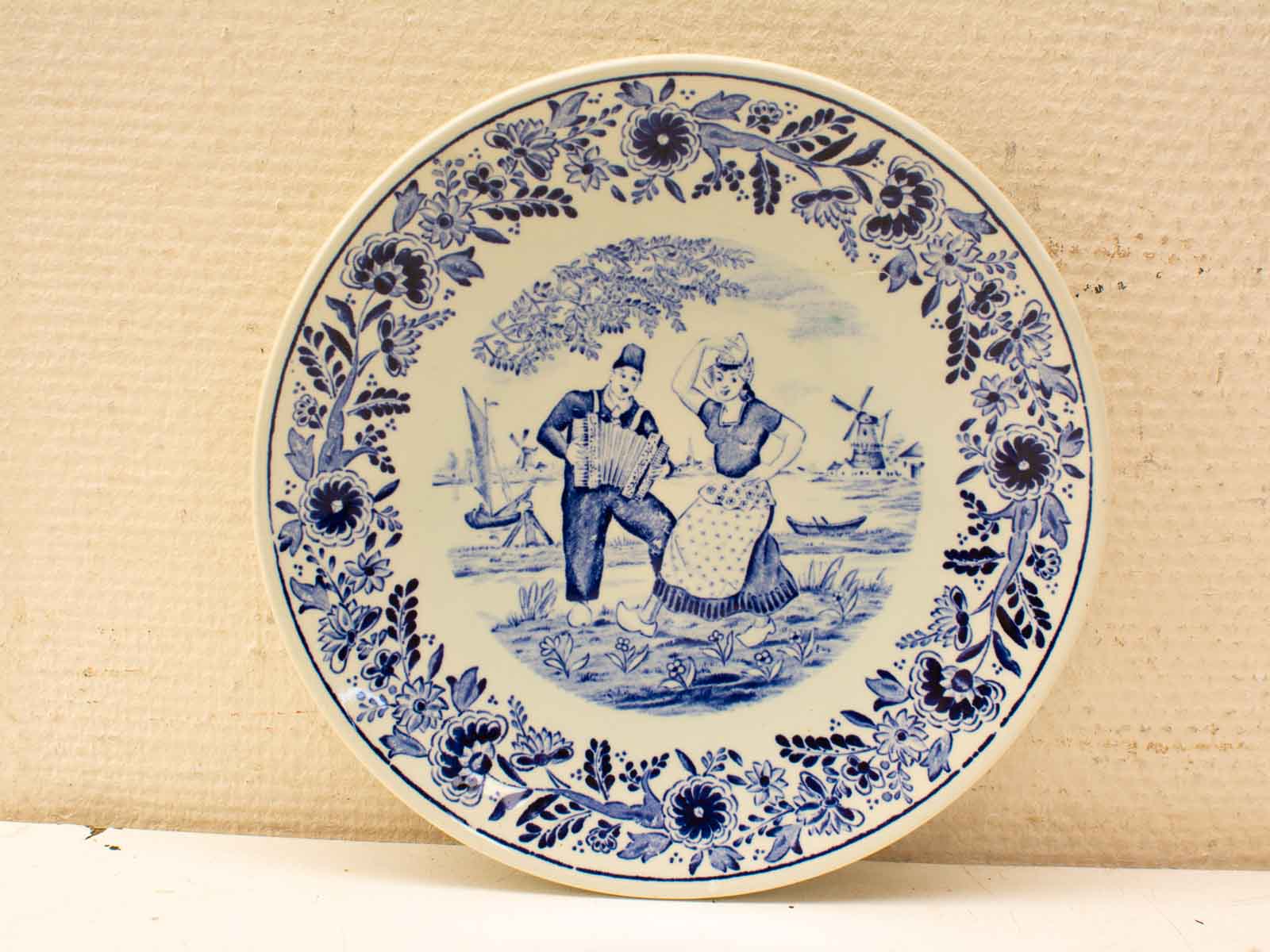 Blue and white decorative plate showcasing a joyful dance scene and Dutch cultural elements.