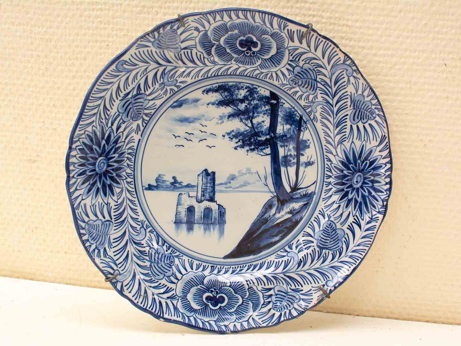 Elegant blue and white decorative plate featuring a serene landscape and floral border.