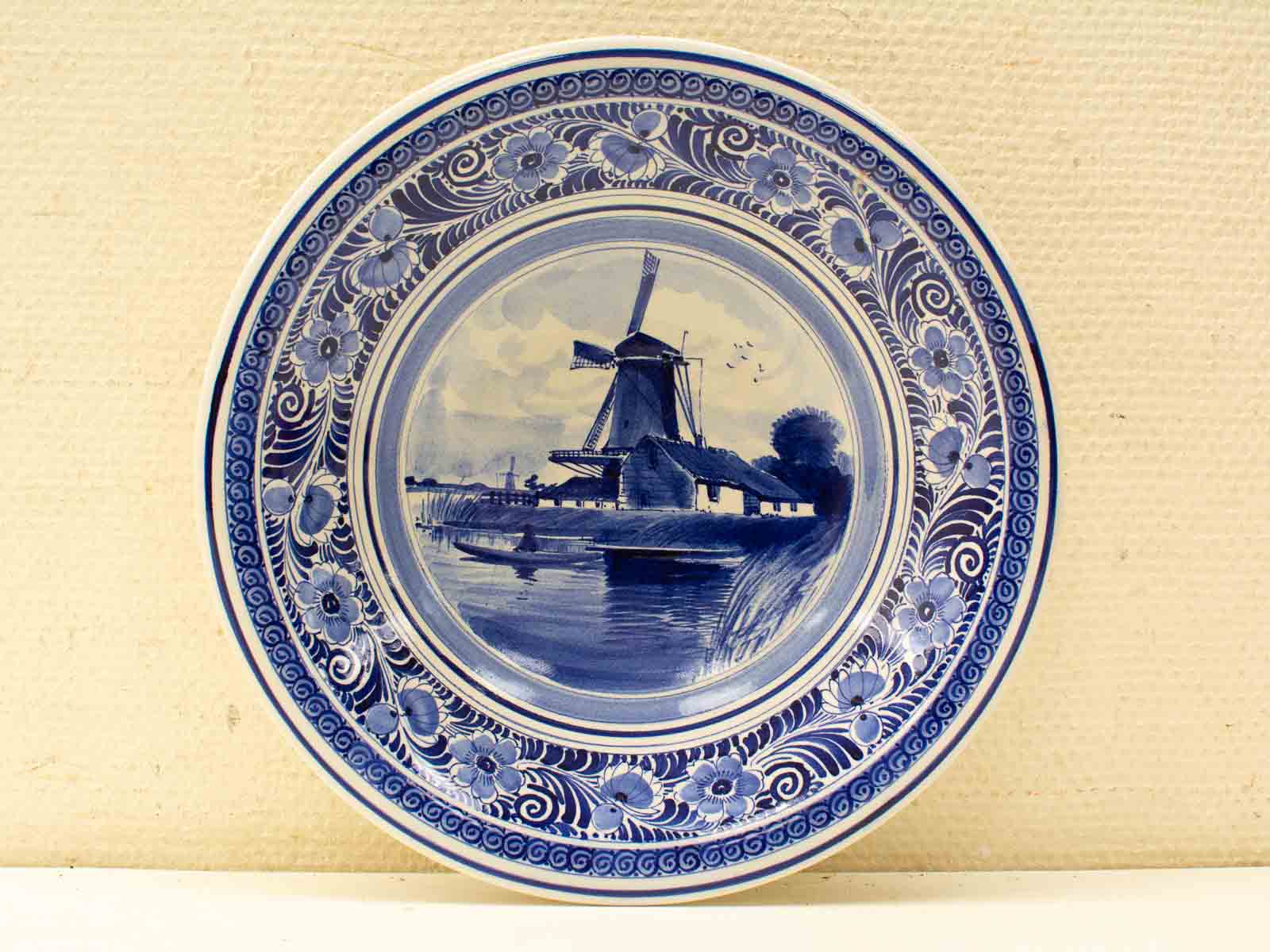 Charming Delftware plate featuring a blue windmill landscape with intricate floral border.