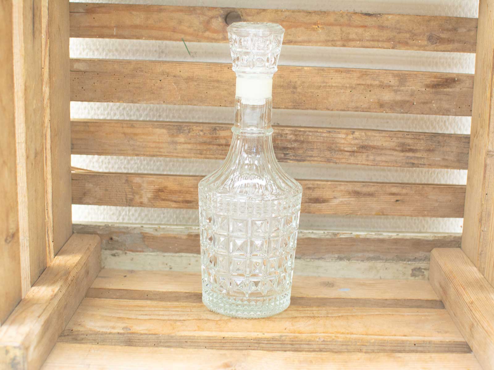 Elegant glass decanter with geometric patterns, set in a rustic wooden crate. Perfect home accent.