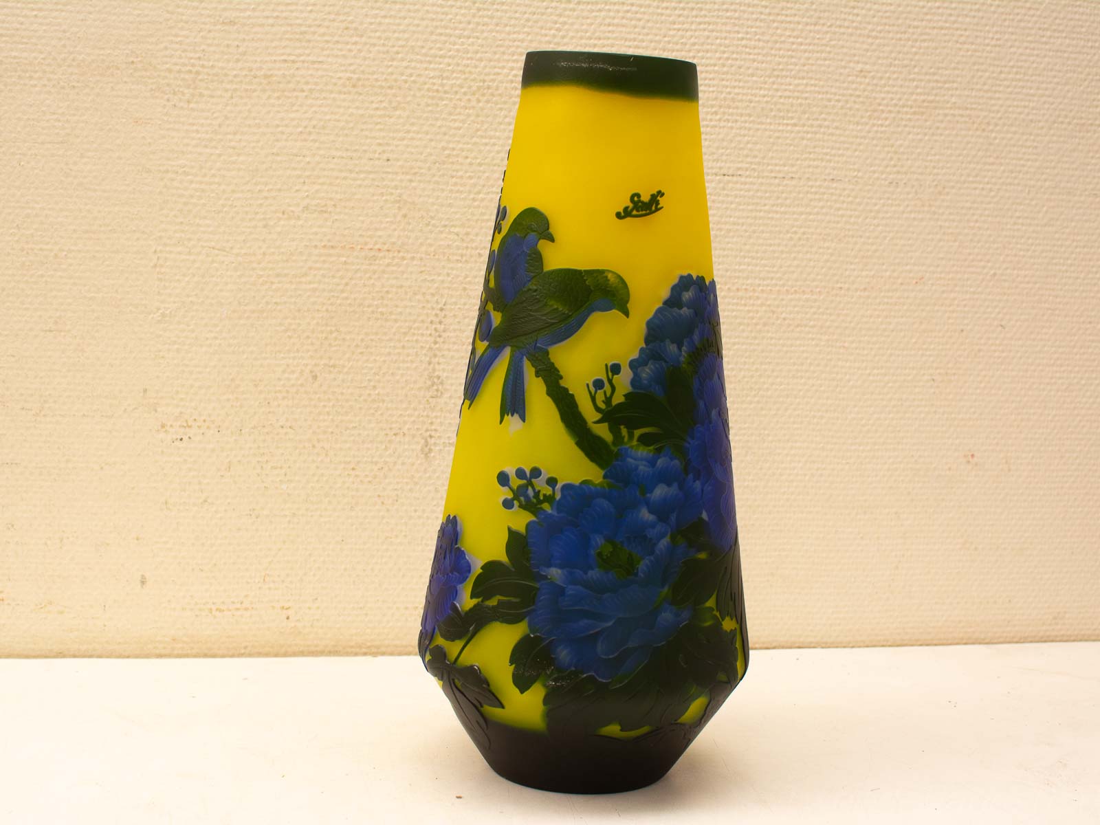 Colorful vintage vase featuring blue flowers and green birds against a vibrant yellow backdrop.