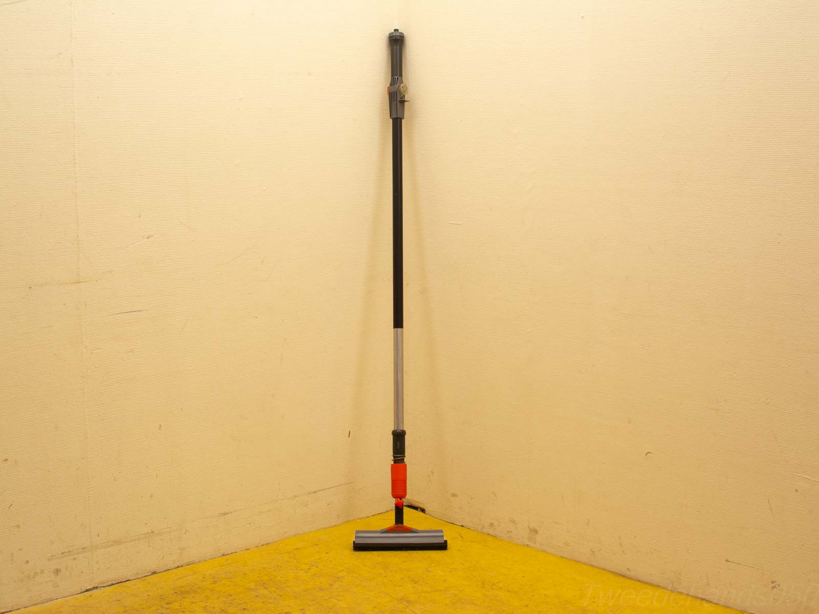 Efficient cleaning tool with triangular head, perfect for corners, on a vibrant yellow floor.