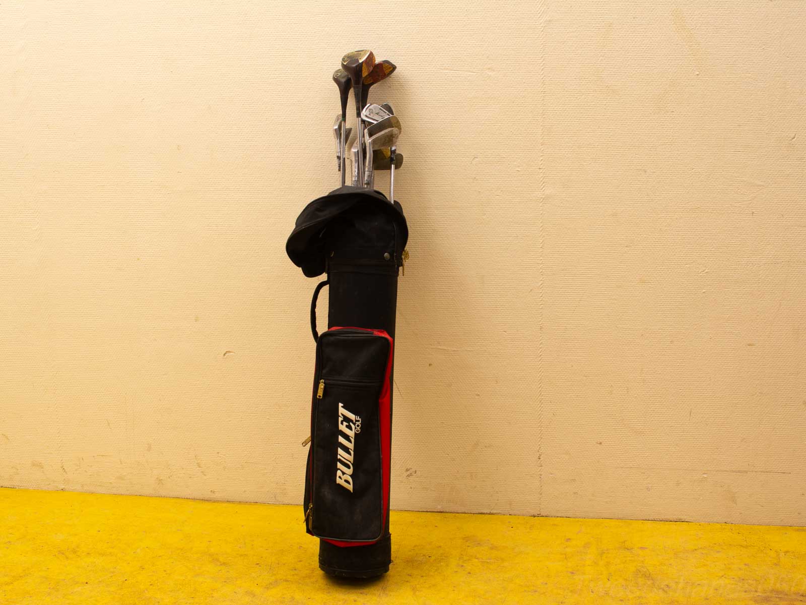 Sleek black and red BULLET golf bag with clubs, ready for a round against a textured wall.