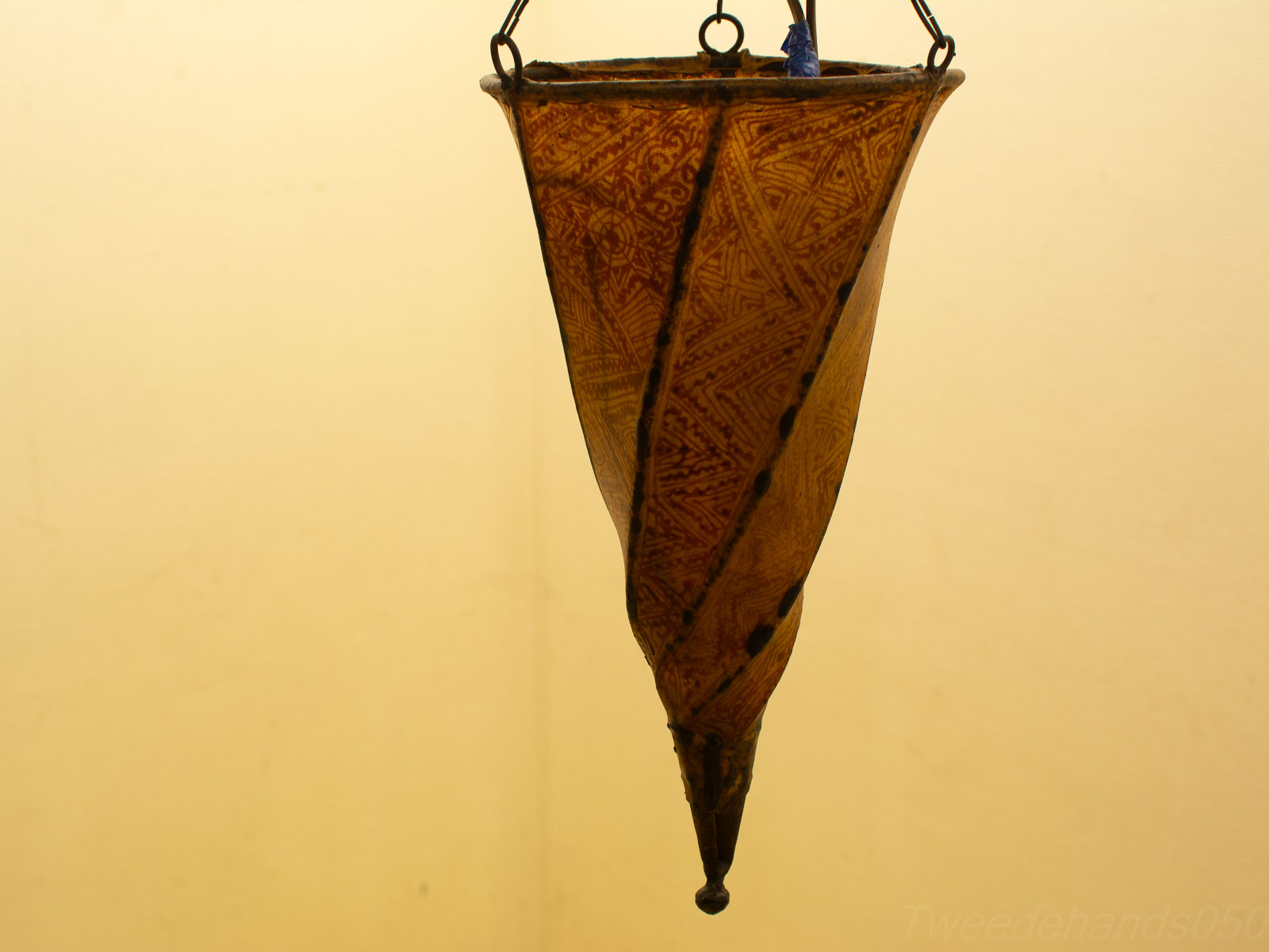 Elegant amber clay vessel with intricate designs, suspended in metal frame.