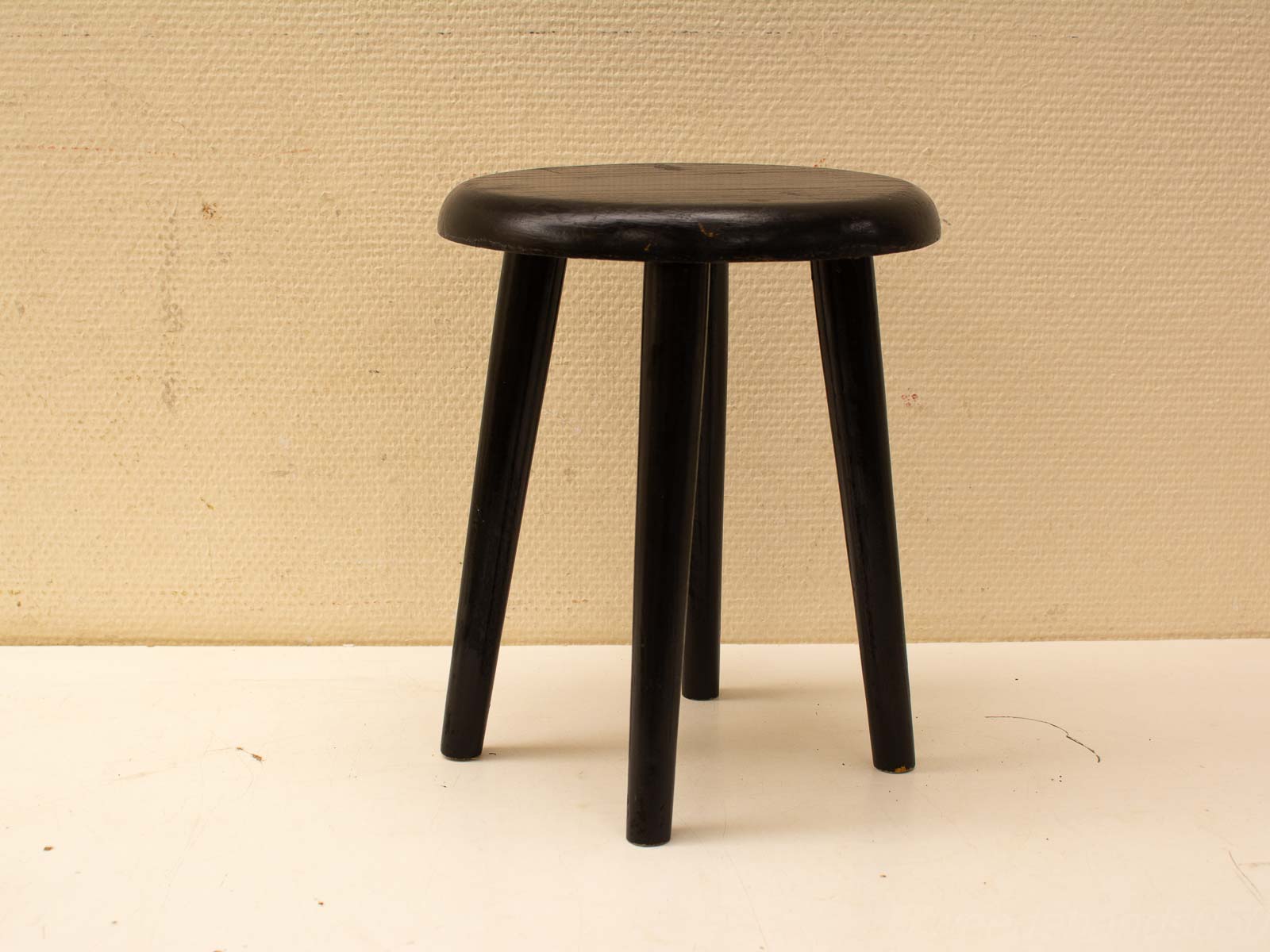 Minimalist black wooden stool with a round seat and slender legs, perfect for versatile spaces.