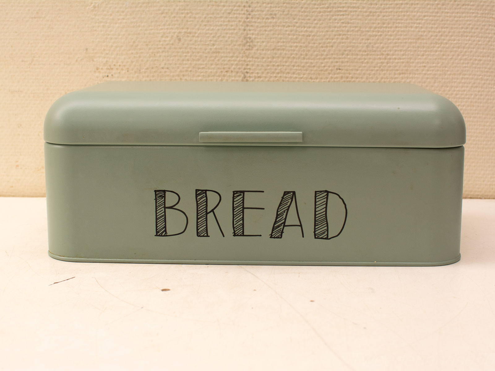 Stylish muted green bread box with playful lettering perfect for modern kitchens.