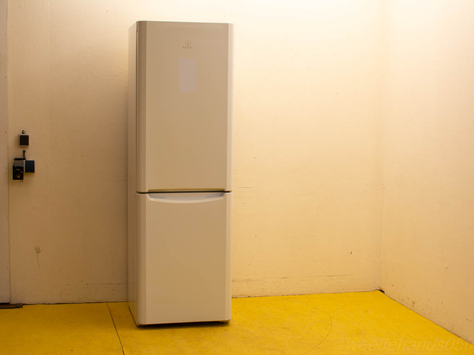 Modern white refrigerator in a minimalistic space with beige walls and yellow flooring.