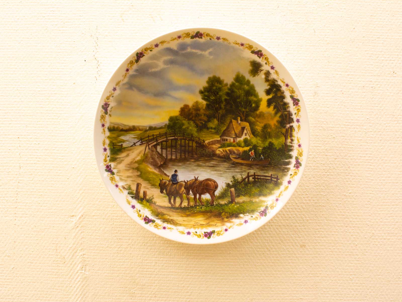 Charming vintage plate depicting a pastoral scene with horses, a river, and a cottage.