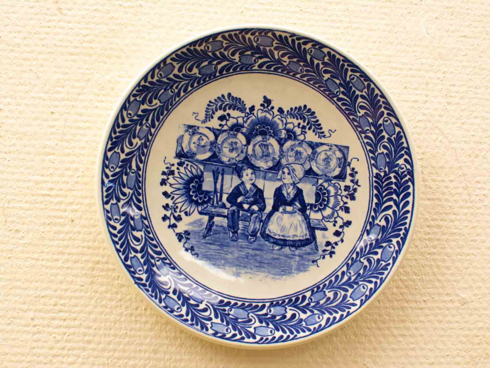 Charming blue and white plate featuring children on a bench with intricate floral designs.