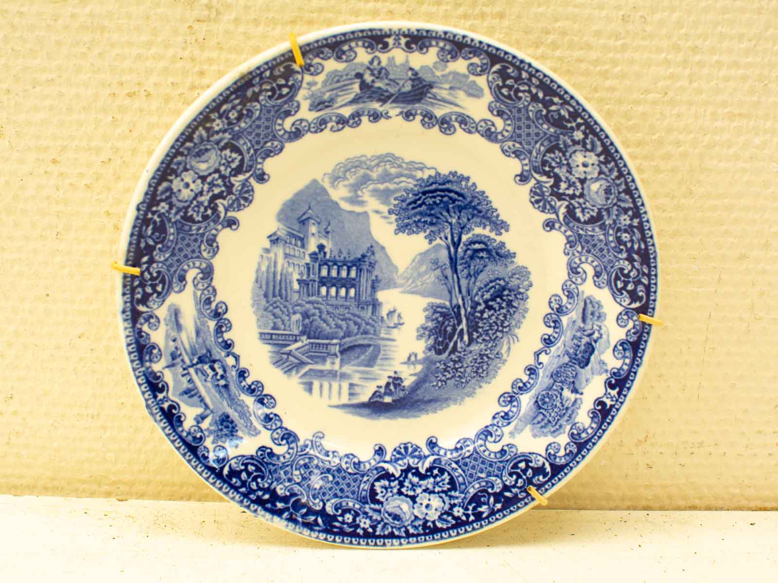 Elegant blue-and-white decorative plate featuring a serene landscape and intricate floral border.