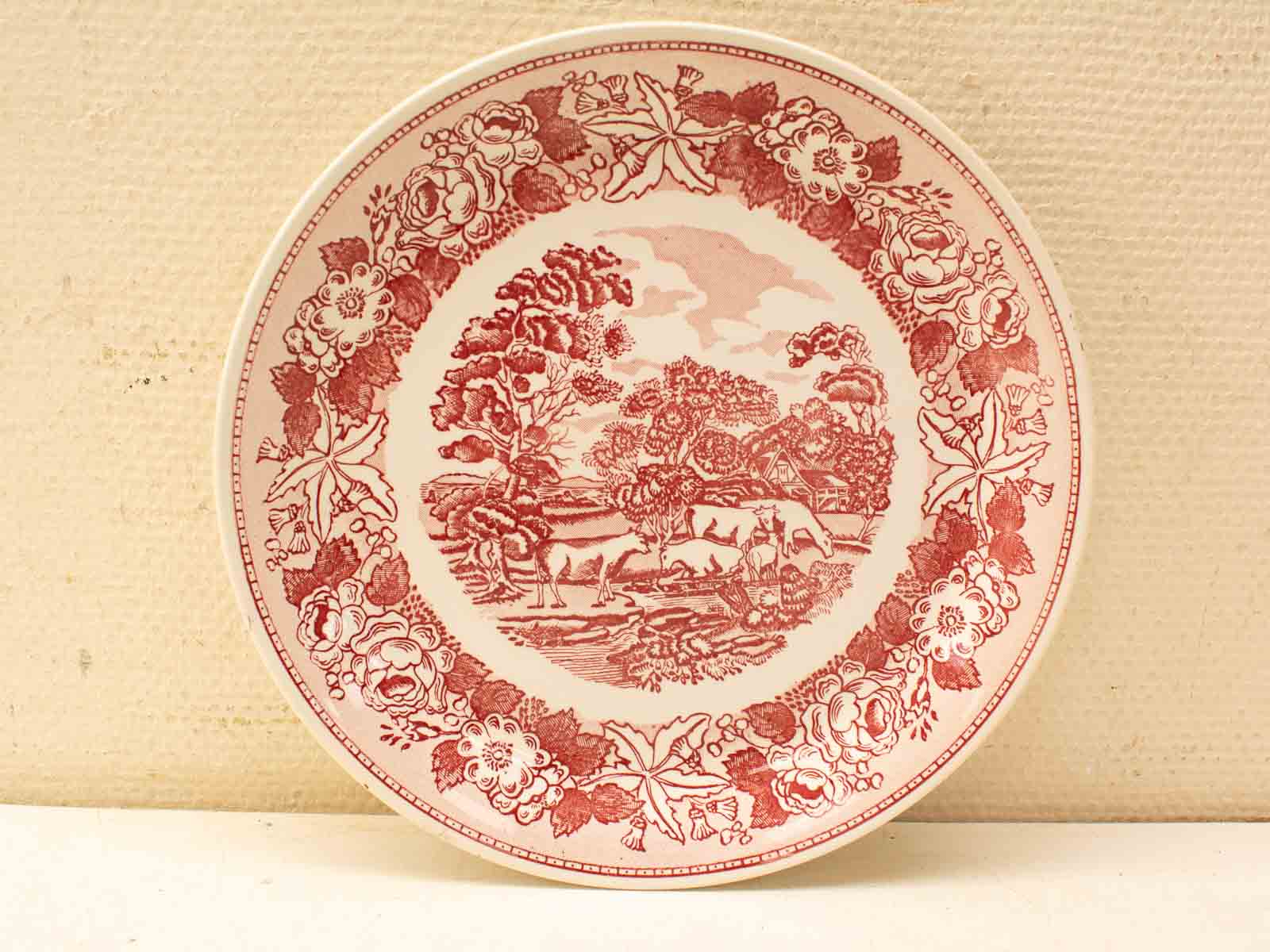 Antique red and white porcelain plate depicting a serene pastoral scene with floral border.