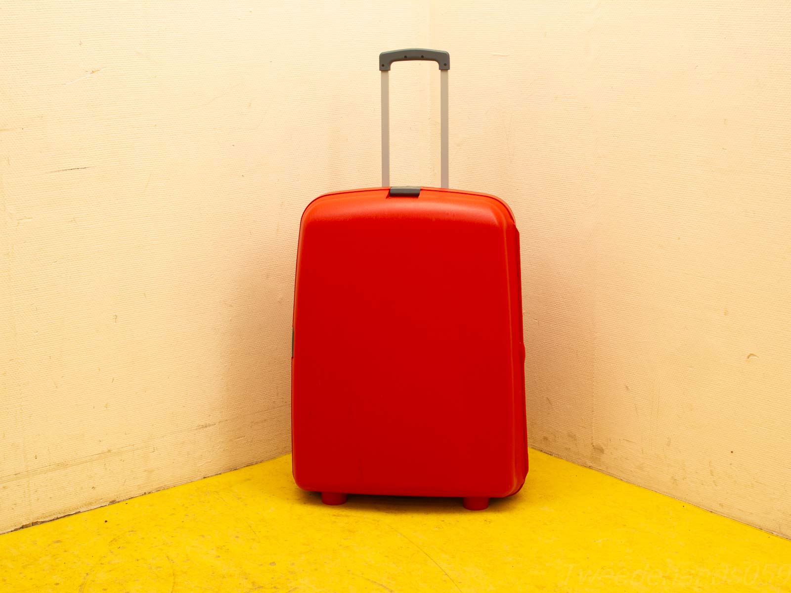 Bright red suitcase in corner, ready for travel against beige wall and yellow floor.