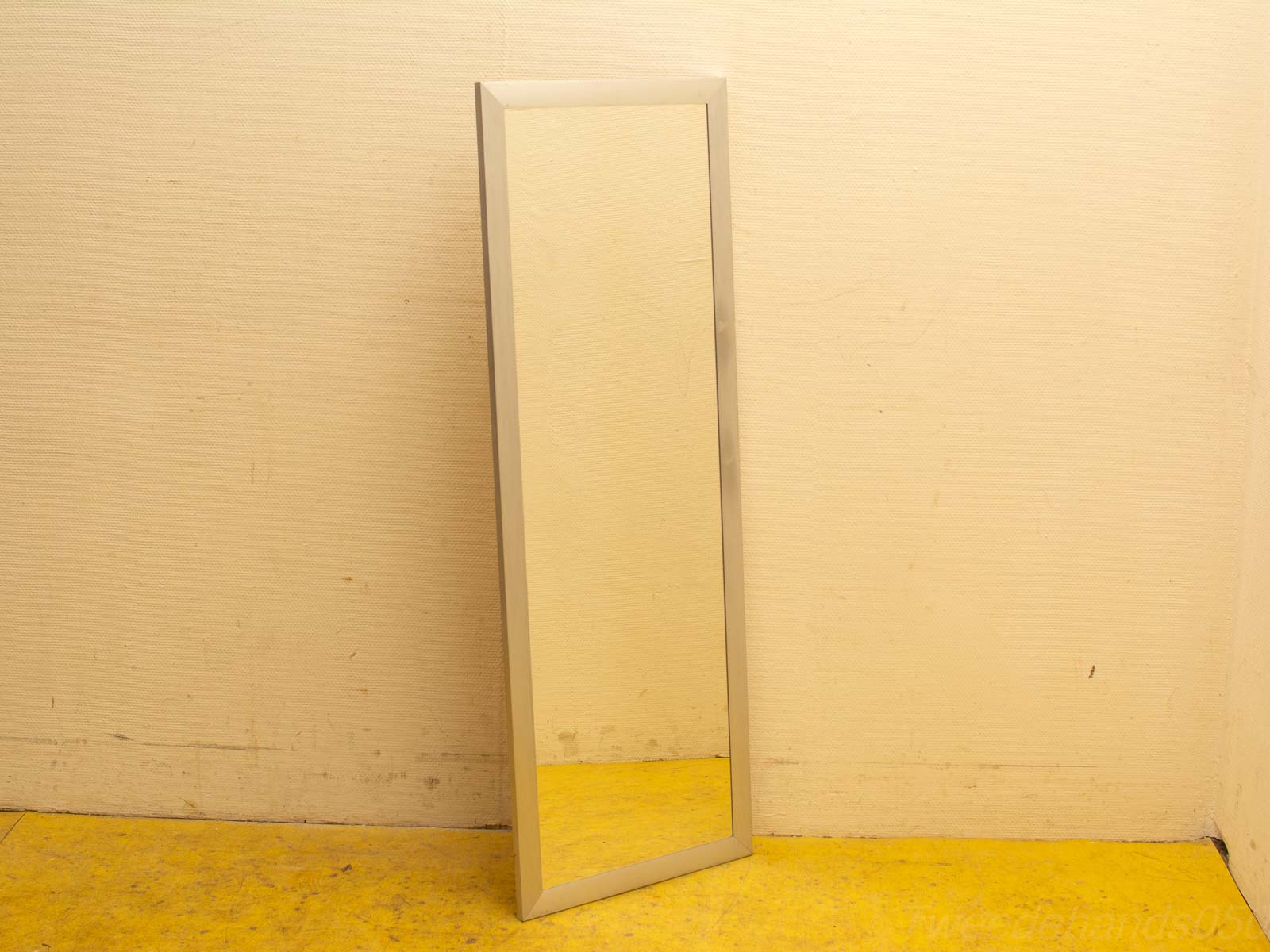 Sleek silver-framed mirror against beige wall with vibrant yellow floor, perfect for full-length views.