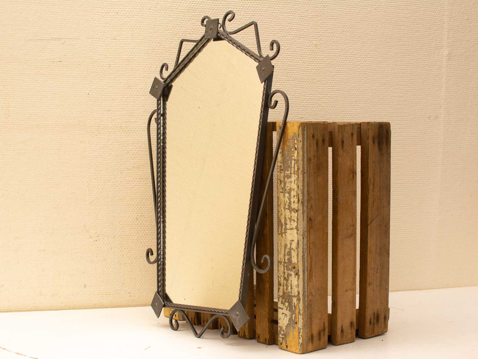 Elegant octagonal mirror with intricate metal frame displayed on a rustic wooden crate.