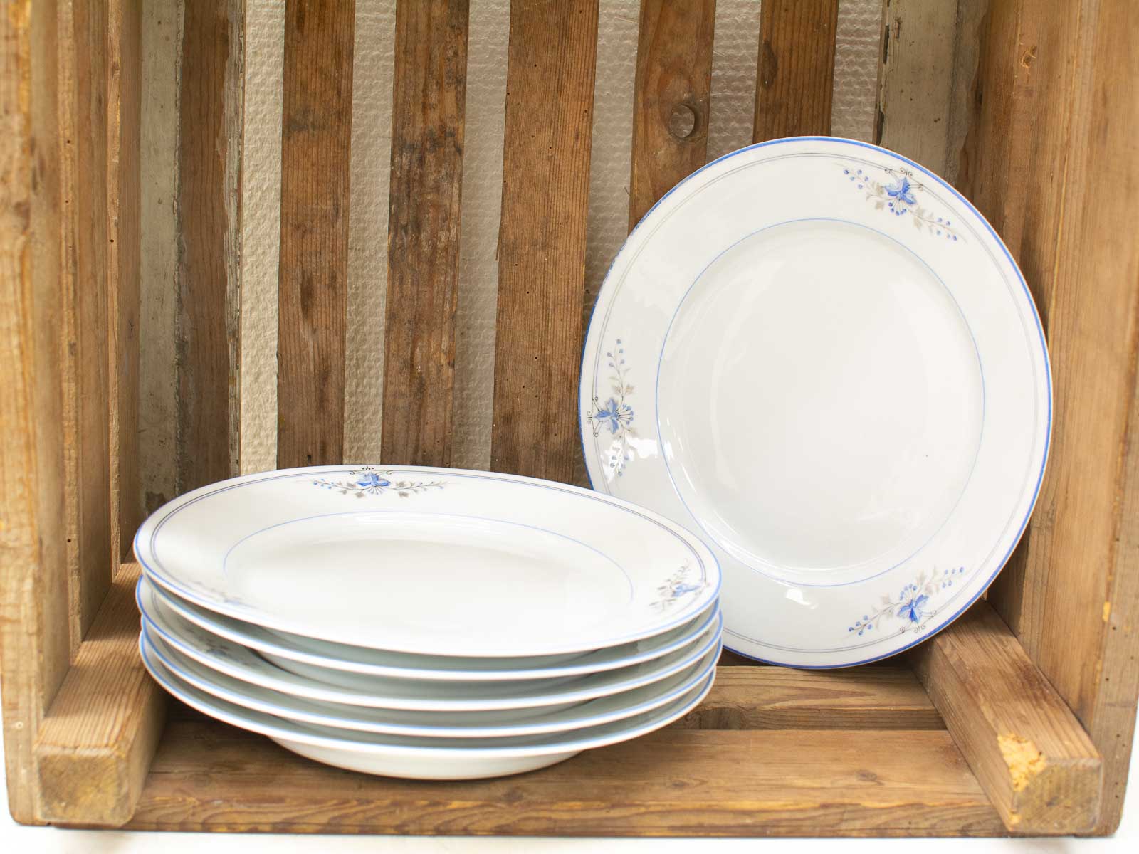 Elegant white plates with blue floral patterns arranged in a rustic wooden crate.