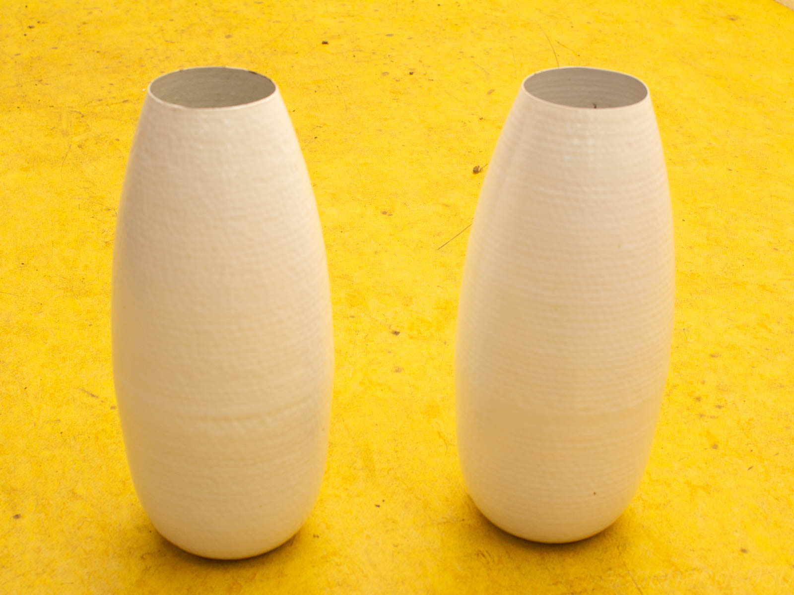 Elegant white vases on a vibrant yellow surface, highlighting modern minimalism and artistic design.