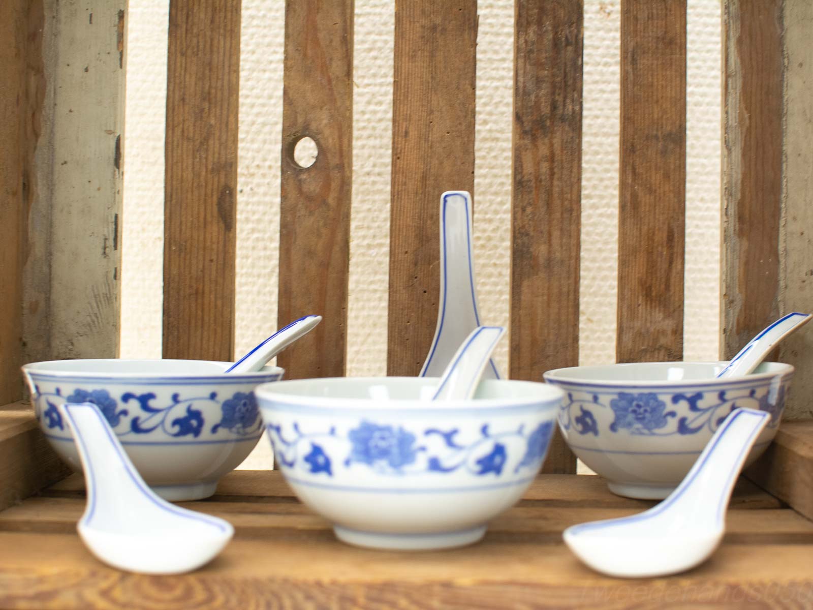 Elegant Chinese porcelain bowls and spoons with blue floral patterns on a rustic wooden background.