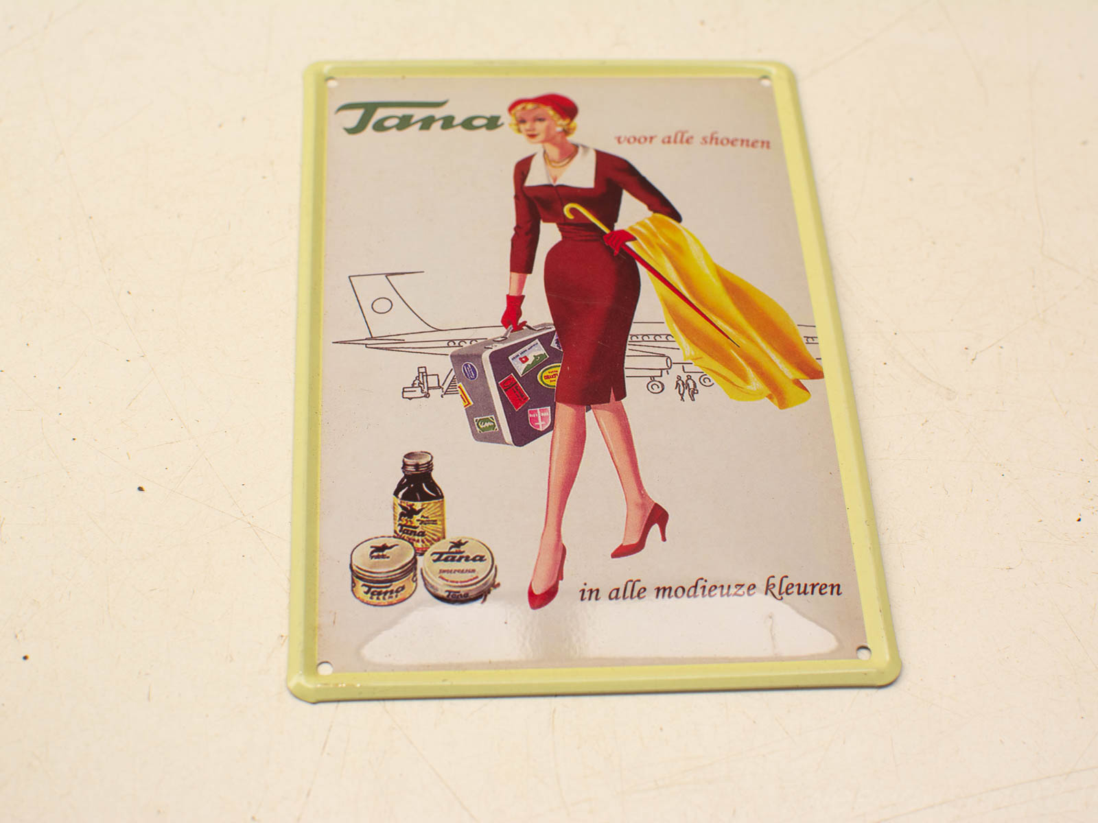 Vintage advertisement featuring a stylish woman, airplane, and Tana shoe care products.