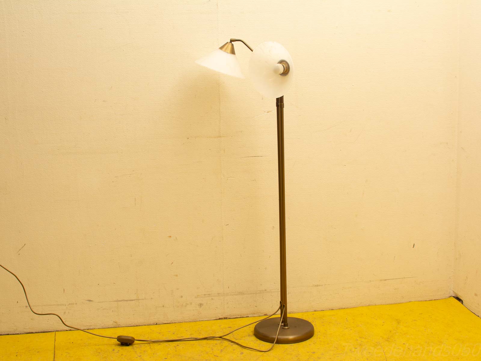 Minimalistische vloerlamp met een moderne lampenkap en warm diffuus licht op gele vloer.