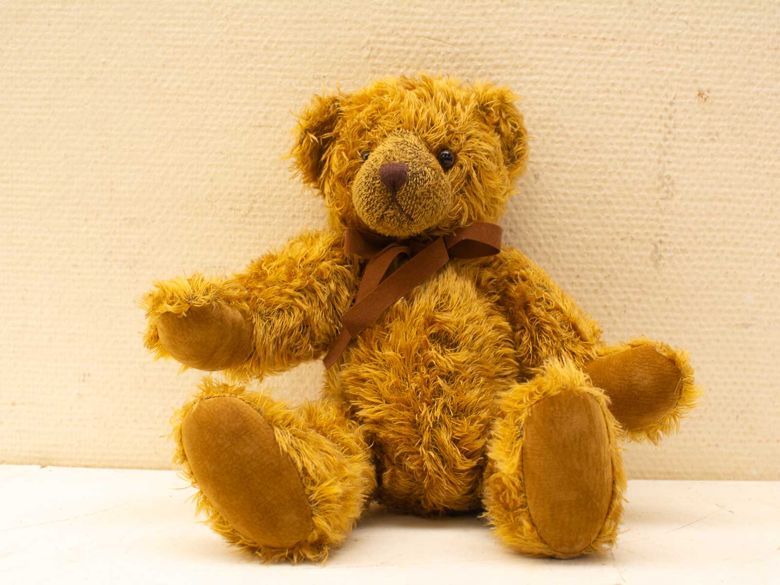 Adorable golden-brown teddy bear with a charming ribbon and inviting smile, perfect for cuddling.