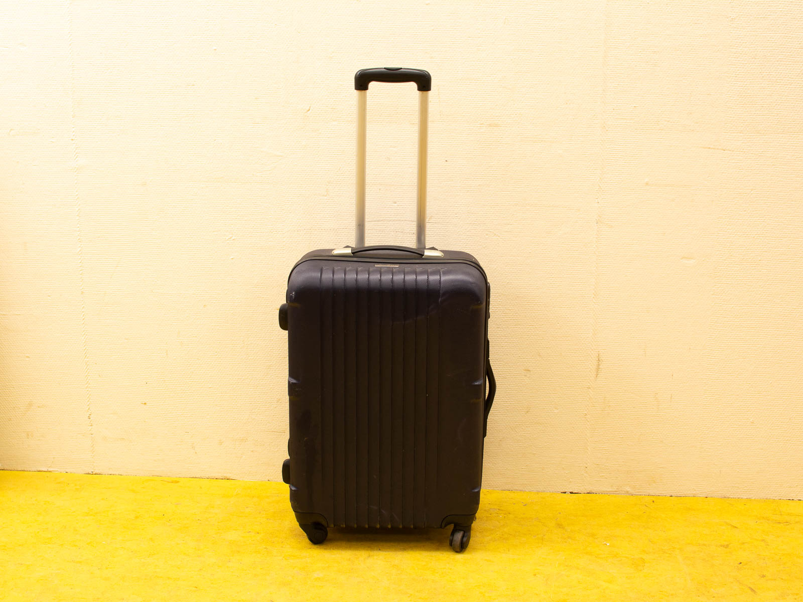 Sleek black suitcase with aluminum handle against a vibrant yellow wall, perfect for travel.