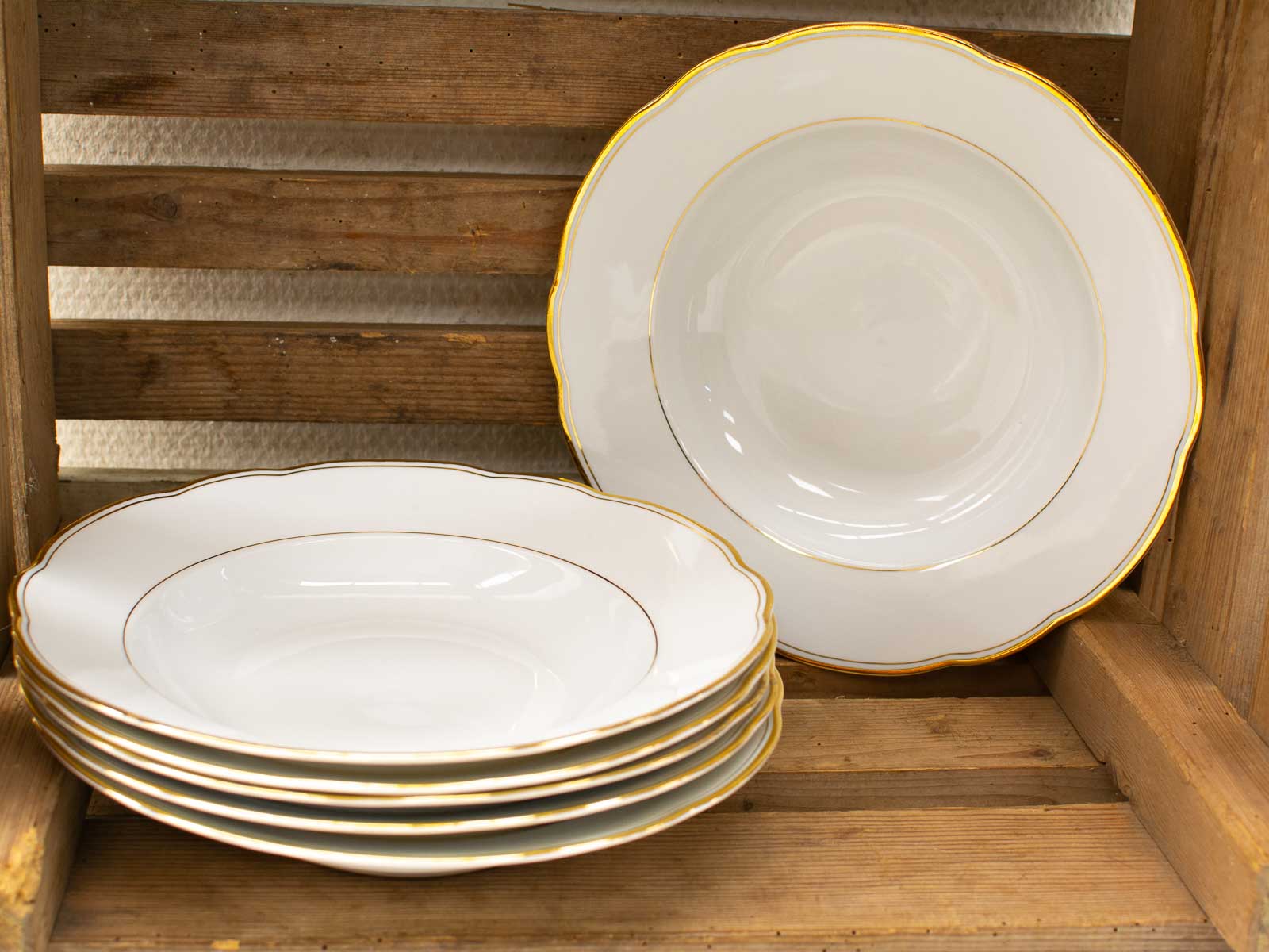 Elegant porcelain plates with gold rims, beautifully arranged on a rustic wooden shelf.