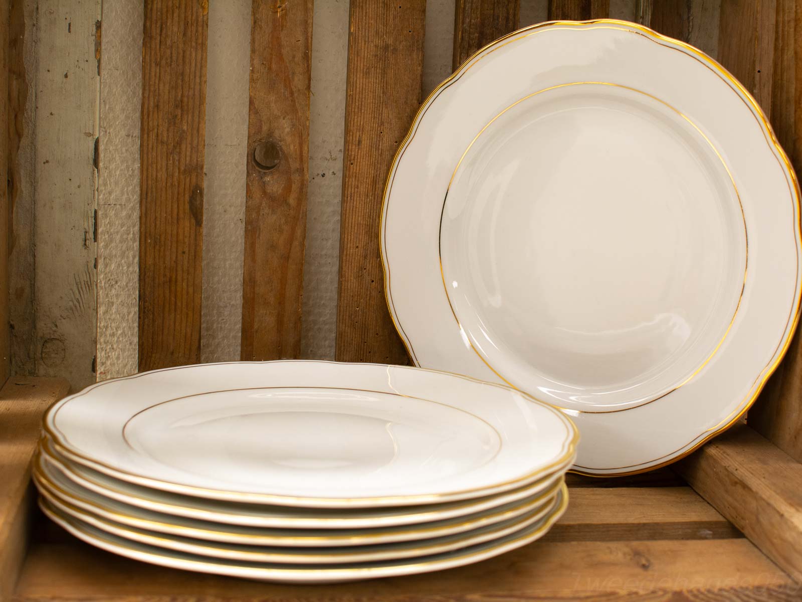 Elegant white plates with gold trim on a rustic wooden table, perfect for upscale dining.