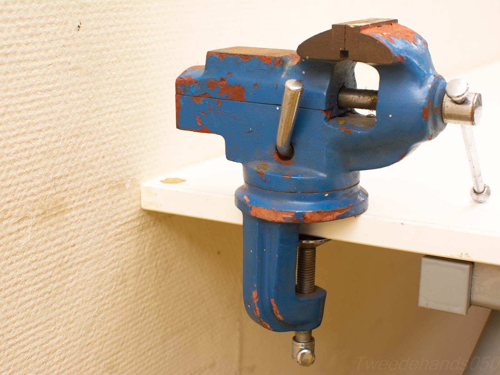 Worn blue workbench vise on beige wall, embodying craftsmanship and durability for DIY projects.