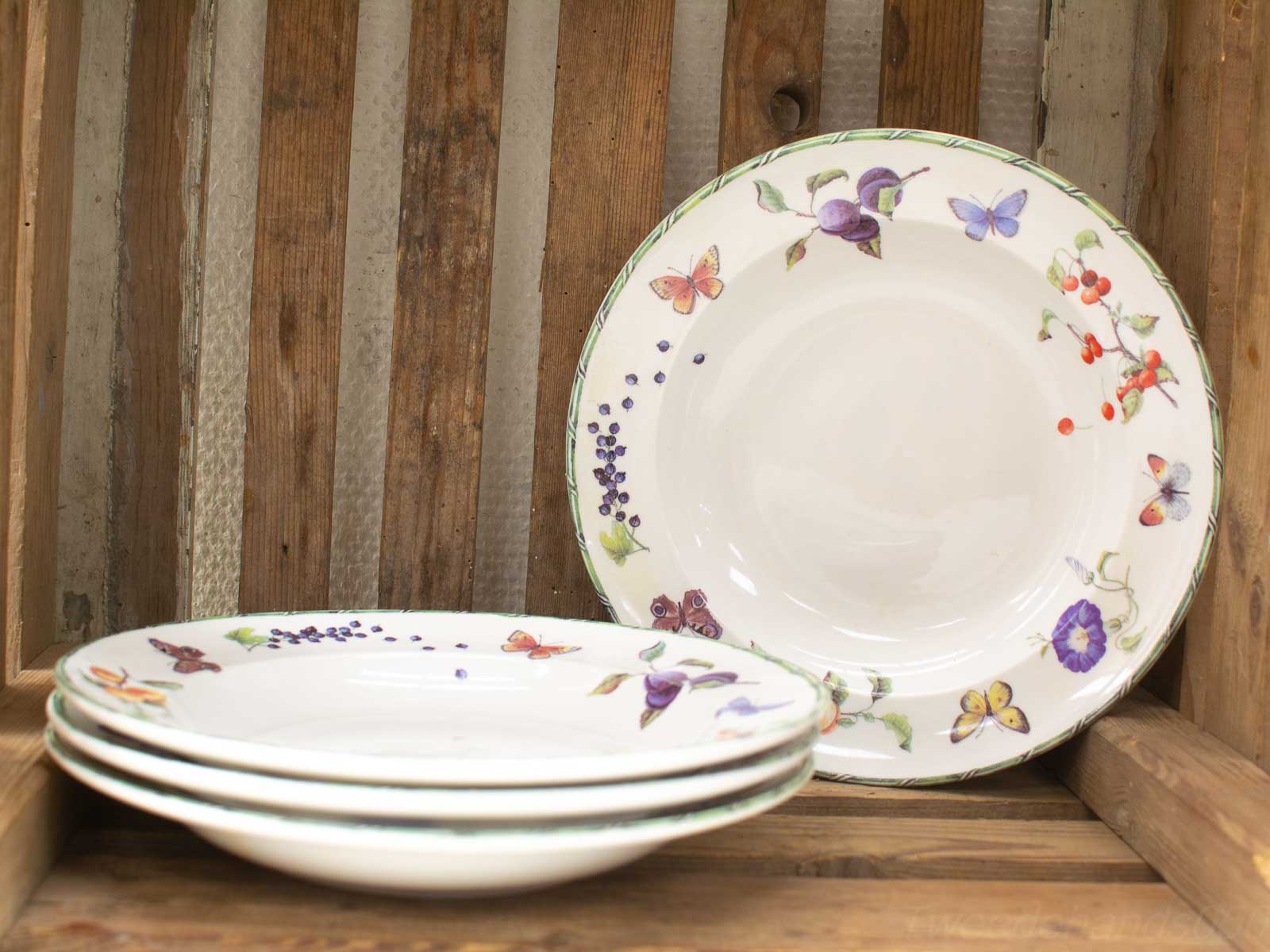 Charming vintage decorative plates in a rustic wooden crate, showcasing floral designs and butterflies.