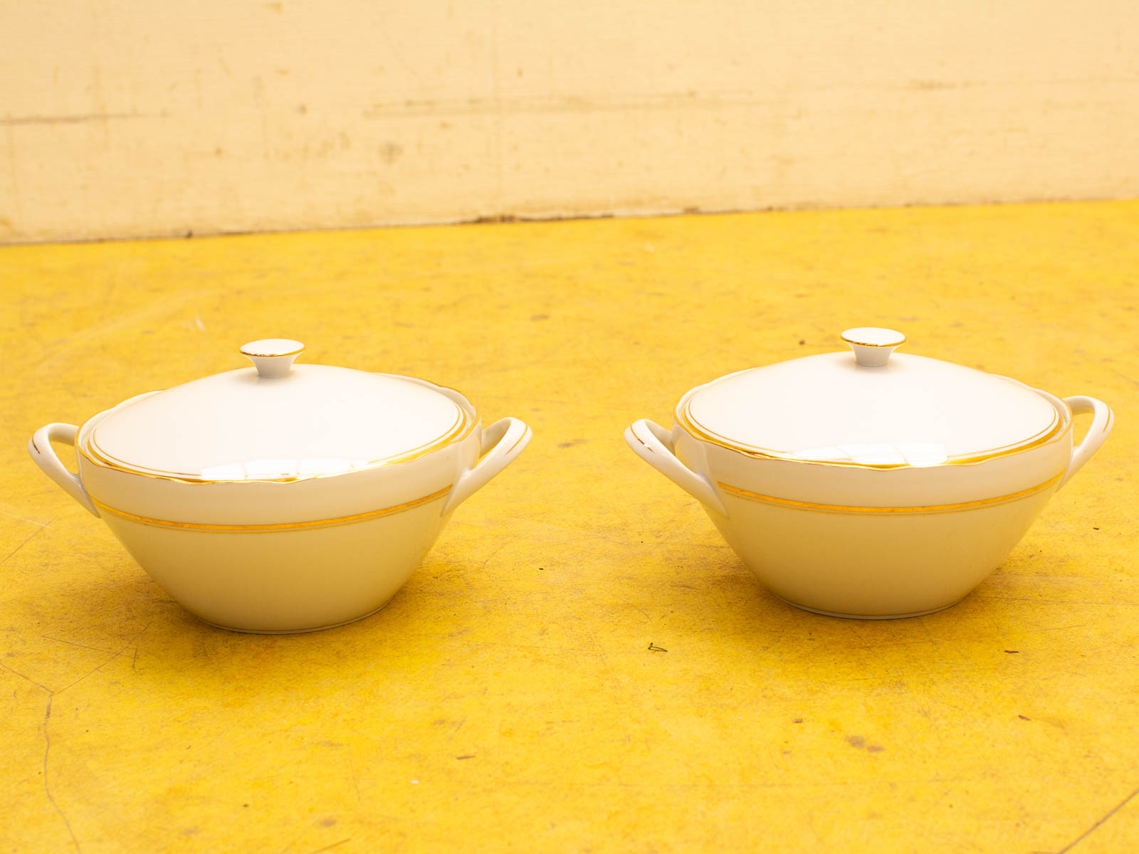 Elegant white porcelain serving dishes with gold trim on a vibrant yellow background.