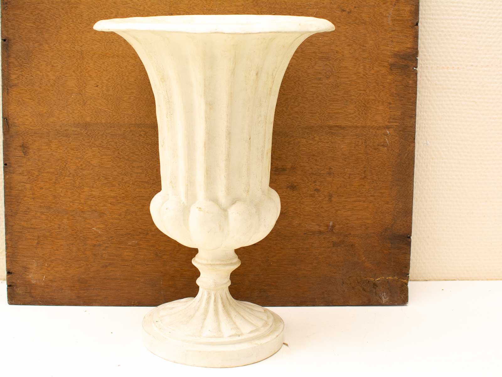 Elegant urn-shaped vase with fluted design and warm wooden background for beautiful decor.