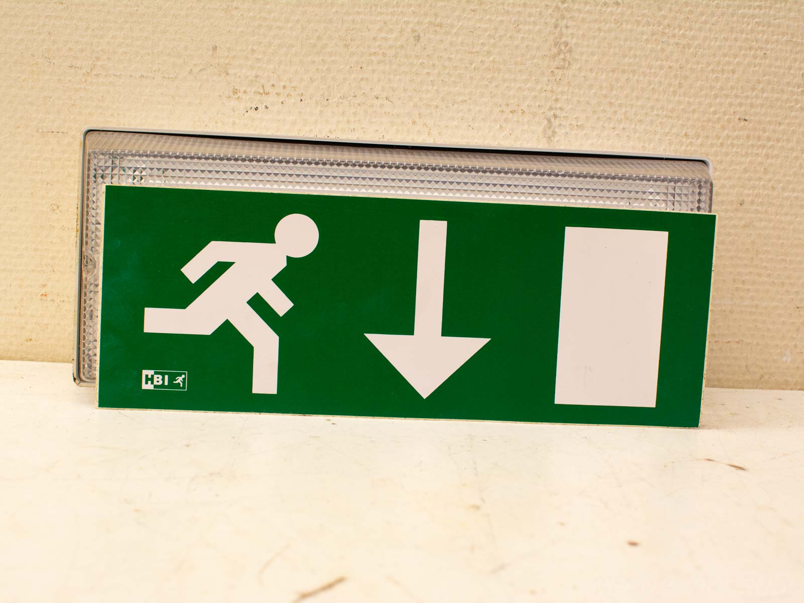 Green emergency exit sign with running figure and downward arrow for quick evacuation guidance.