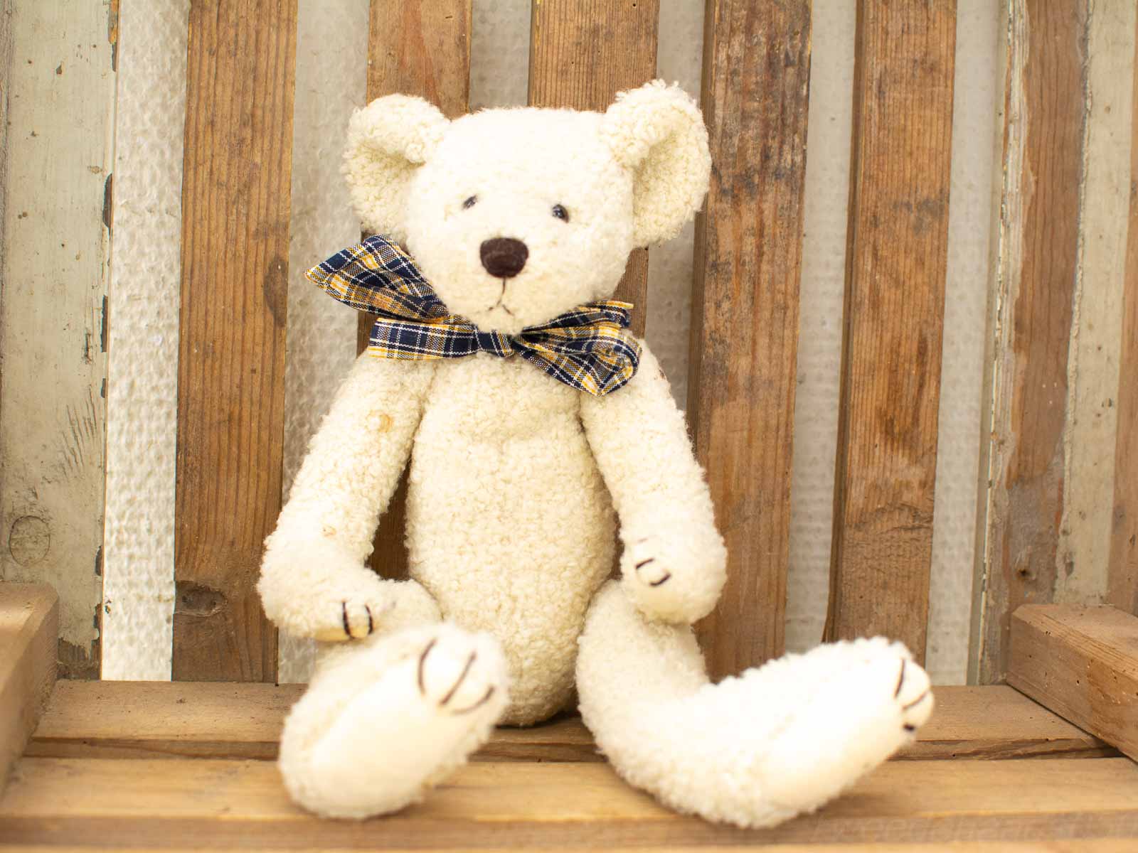 Cozy cream teddy bear with a playful plaid bow tie, perfect for any childs room.