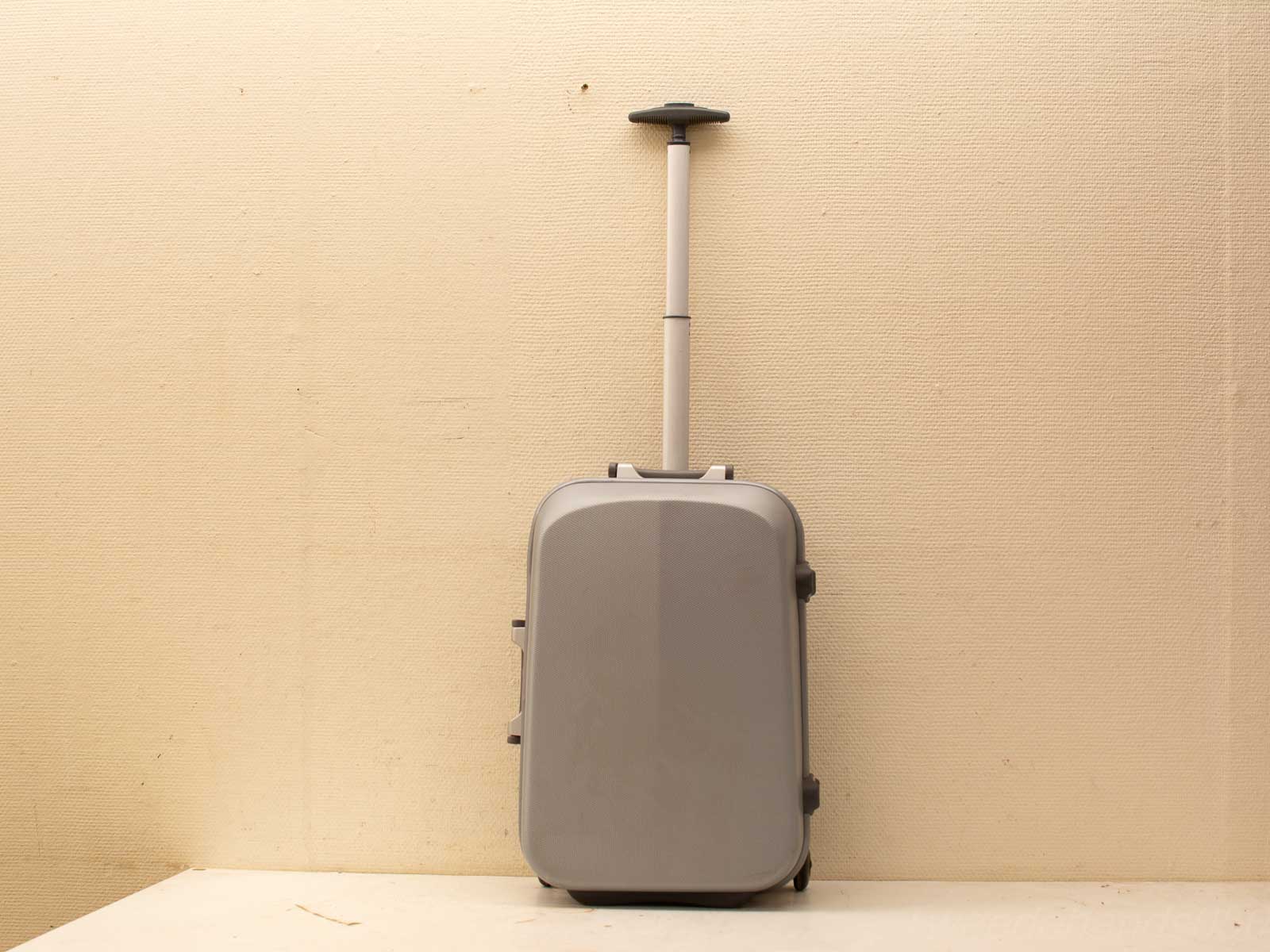 Sleek gray suitcase with wheels and handle, styled against a neutral wall backdrop.