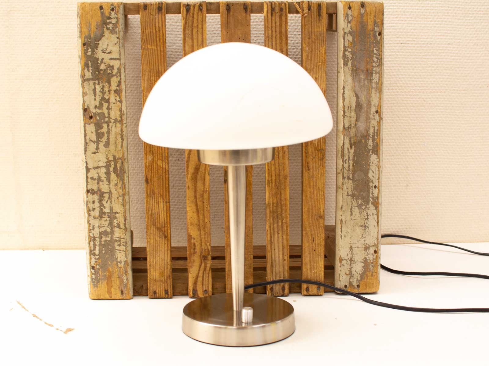 Modern table lamp with white shade against rustic wooden backdrop, blending contemporary and vintage styles.