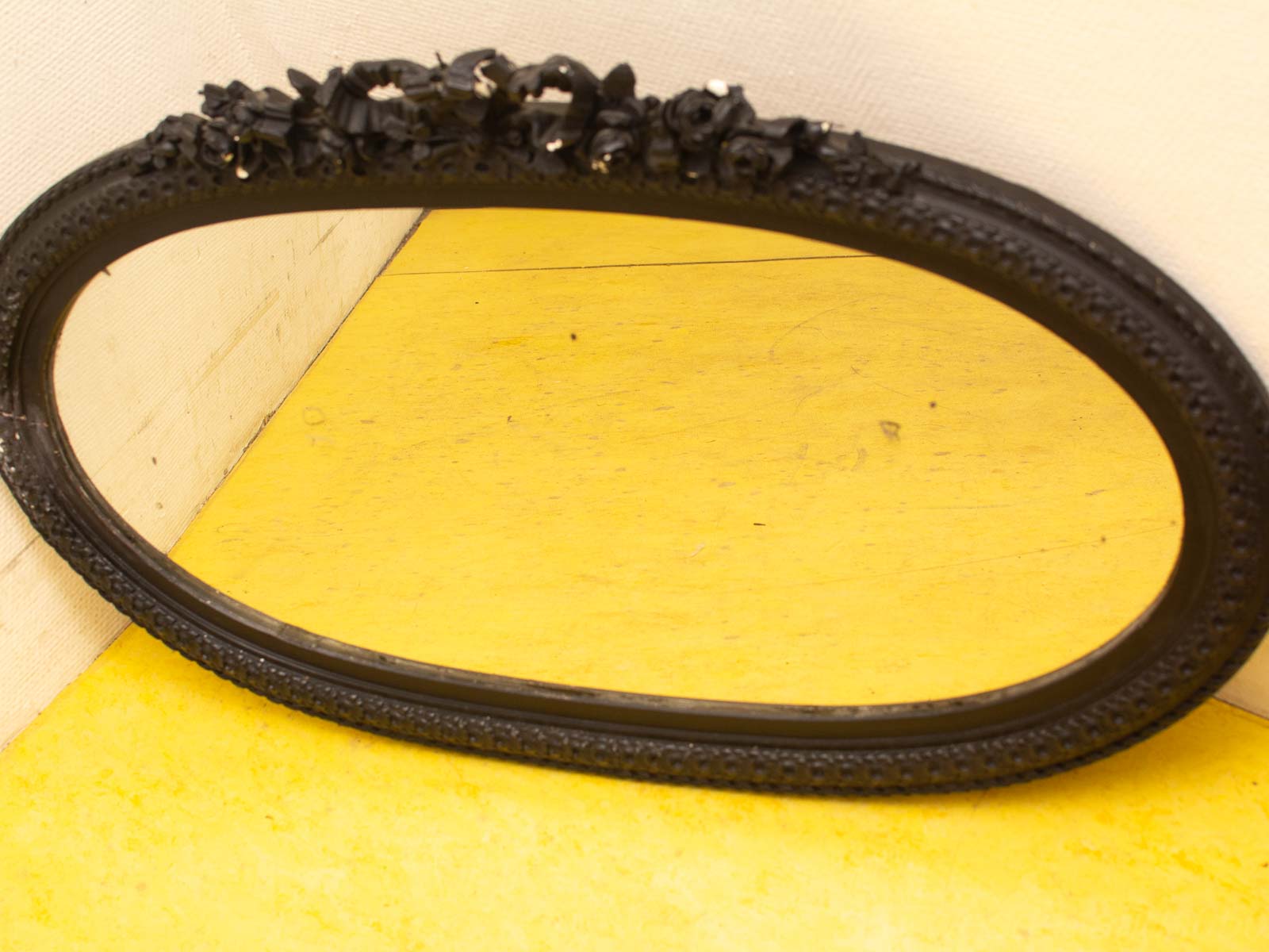 Elegant vintage oval mirror with ornate black frame on vibrant yellow floor. Perfect decor accent.