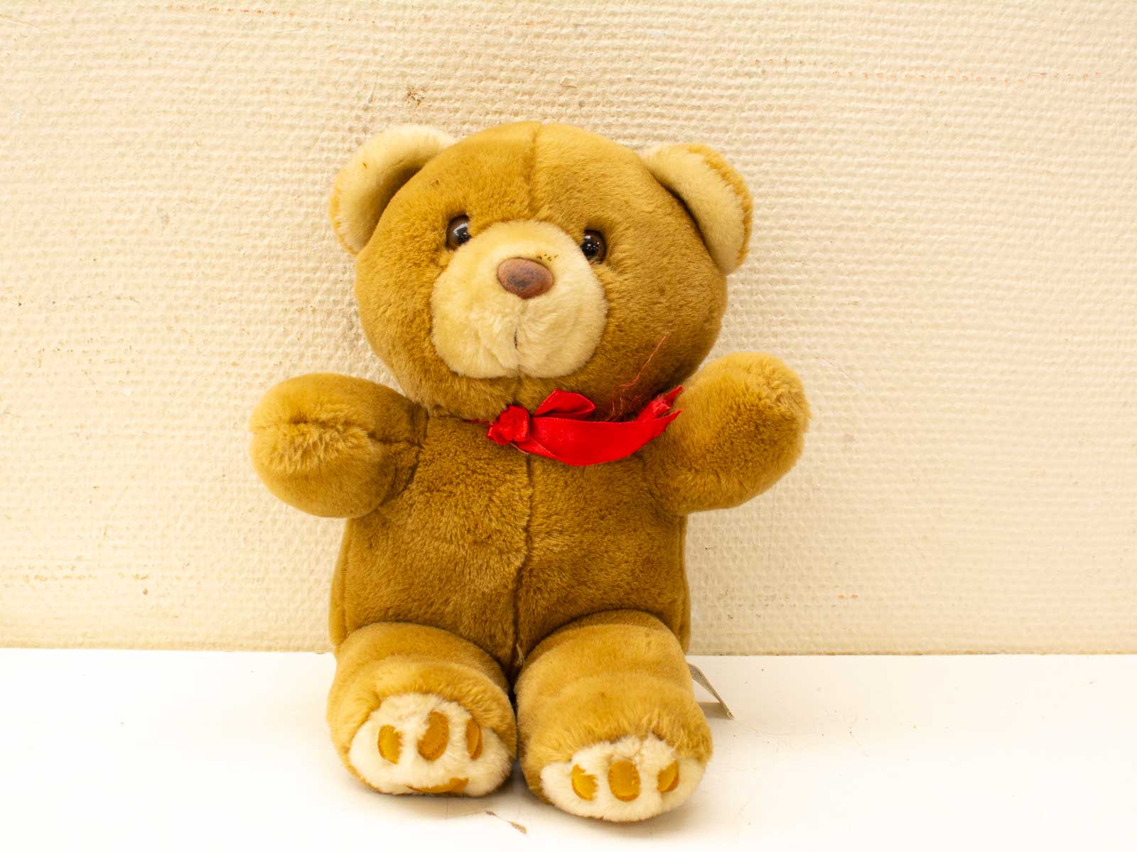 Adorable secondhand teddy bear with a red ribbon, perfect for hugs and nostalgic memories.