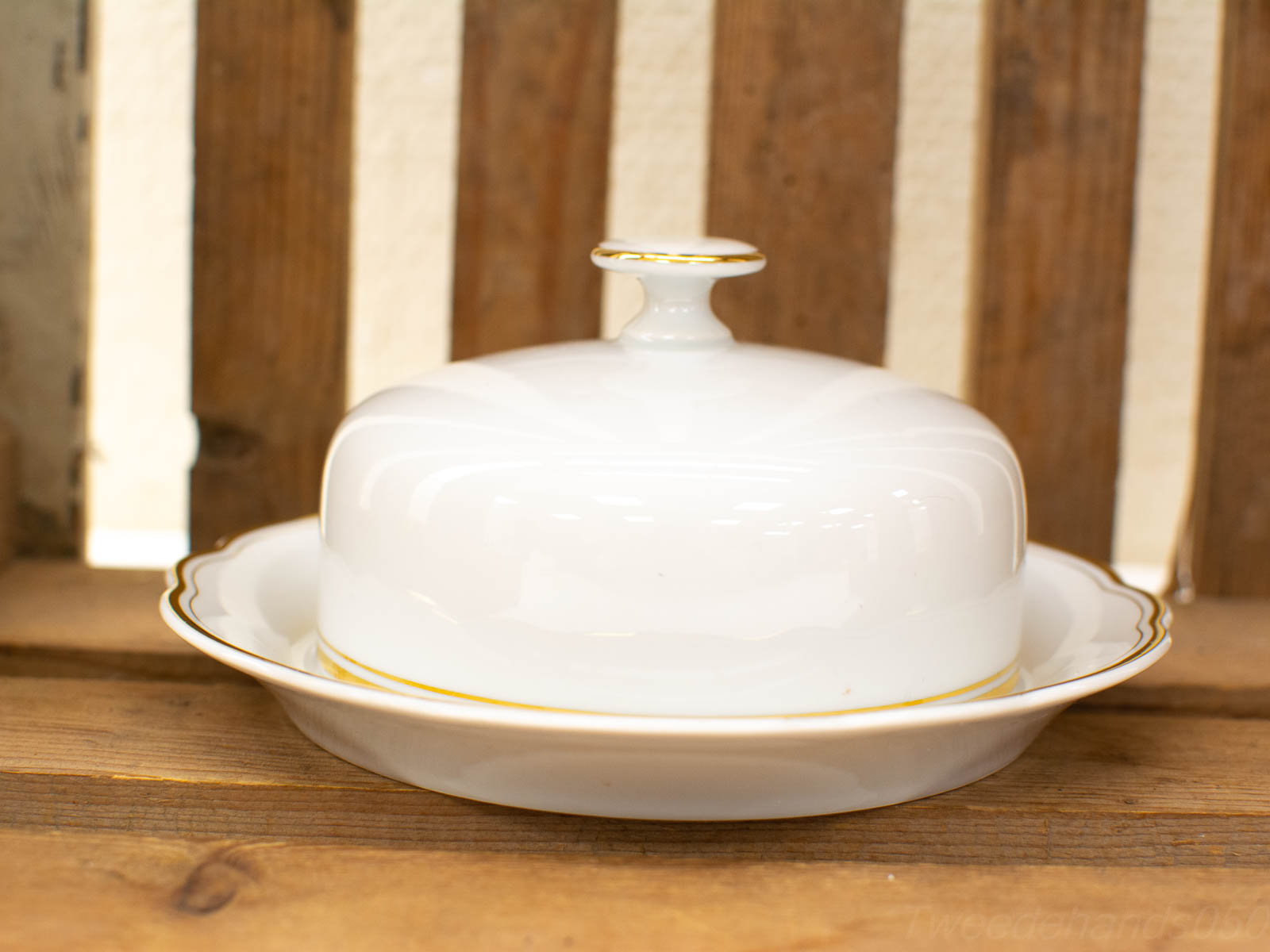 Elegant porcelain butter dish with gold trim on a rustic wooden backdrop.