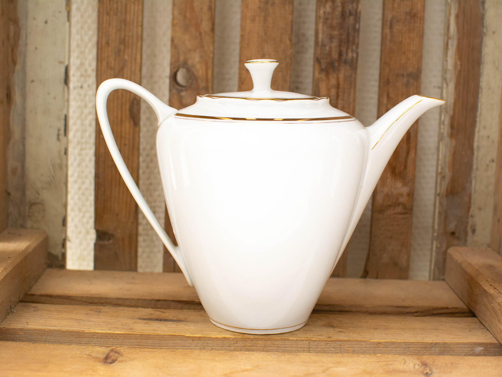 Elegant white porcelain teapot with gold trim on rustic wood, perfect for stylish tea gatherings.