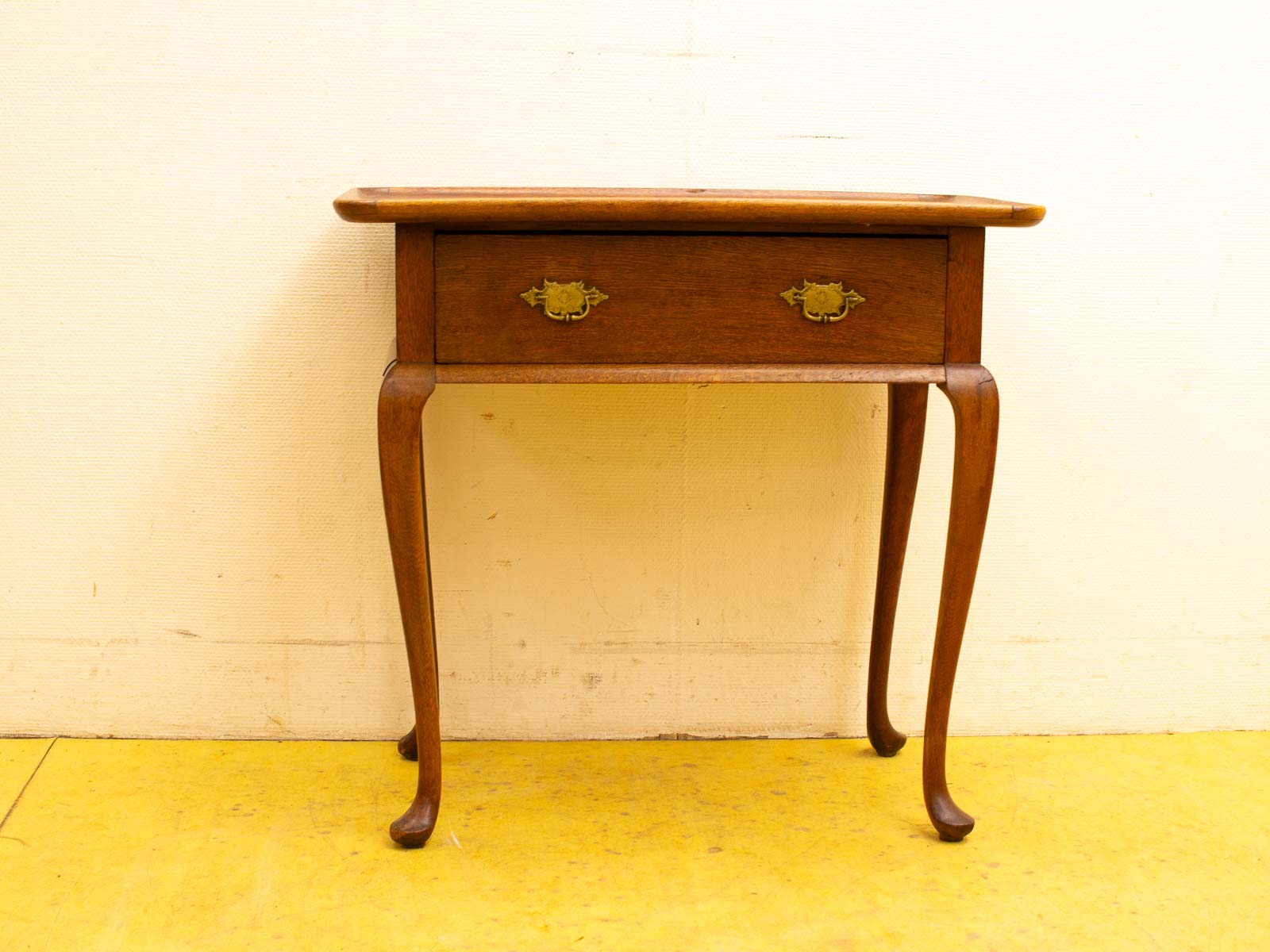 Elegant wooden side table with polished finish, vintage brass handle, and gracefully tapered legs.