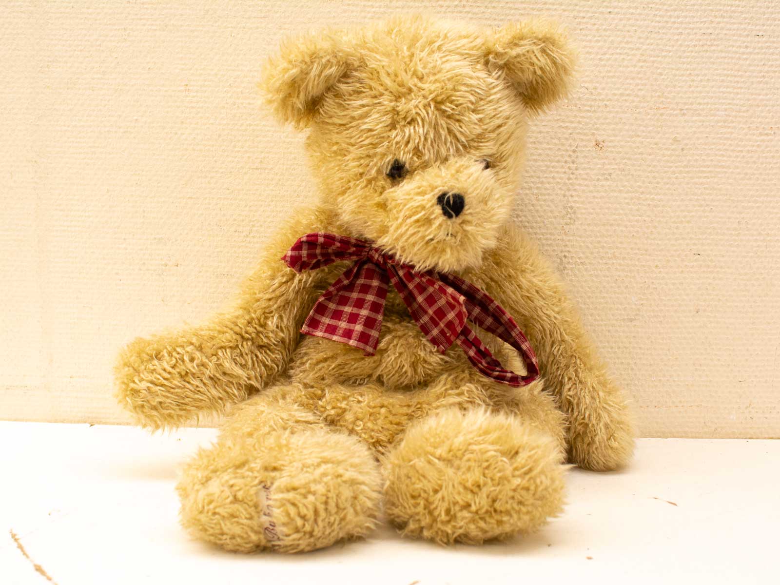 Charming vintage teddy bear with soft beige fur and a cheerful red checkered bow.