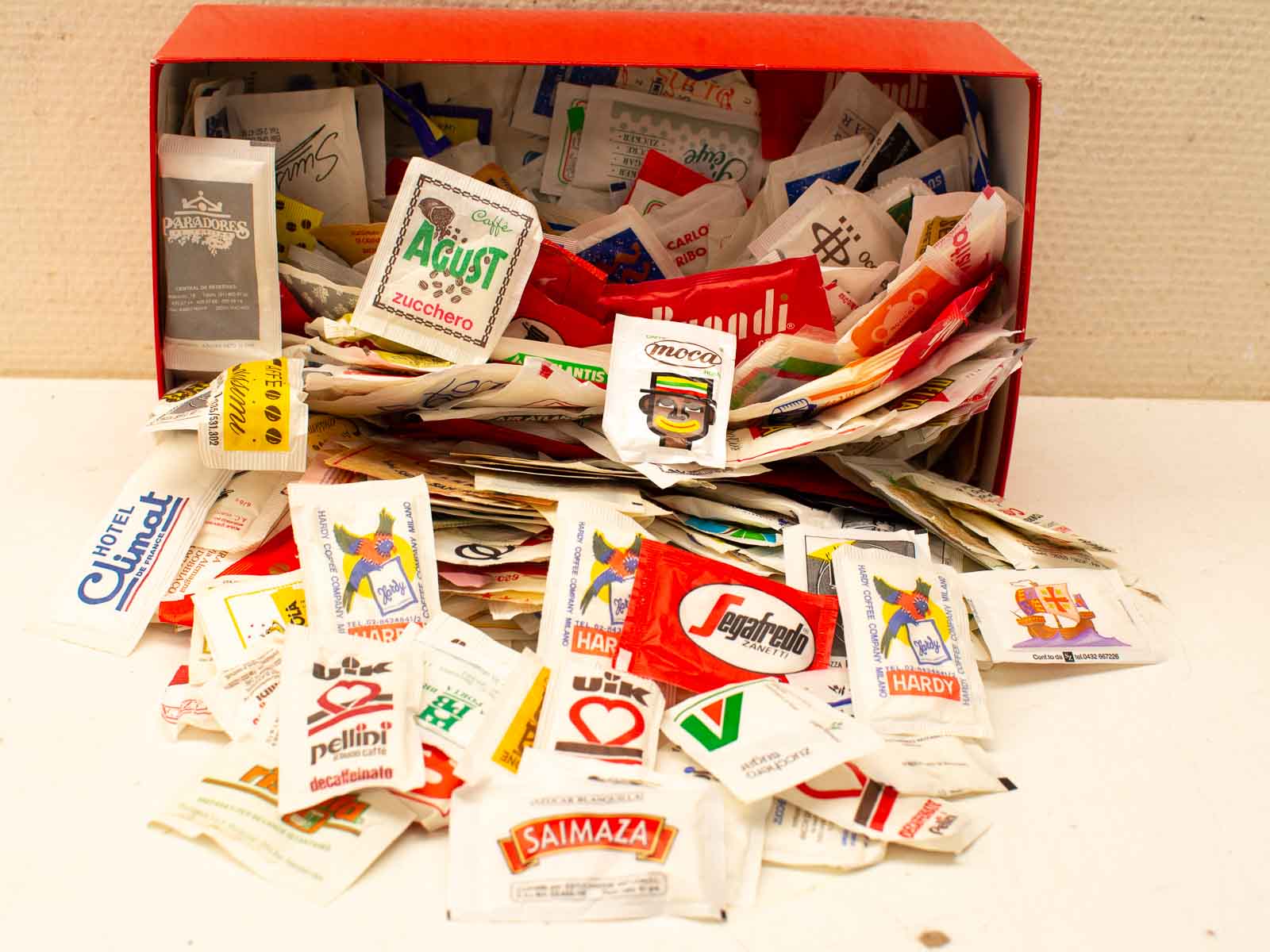 Colorful sugar and coffee packets spill from a red container, celebrating global coffee culture.