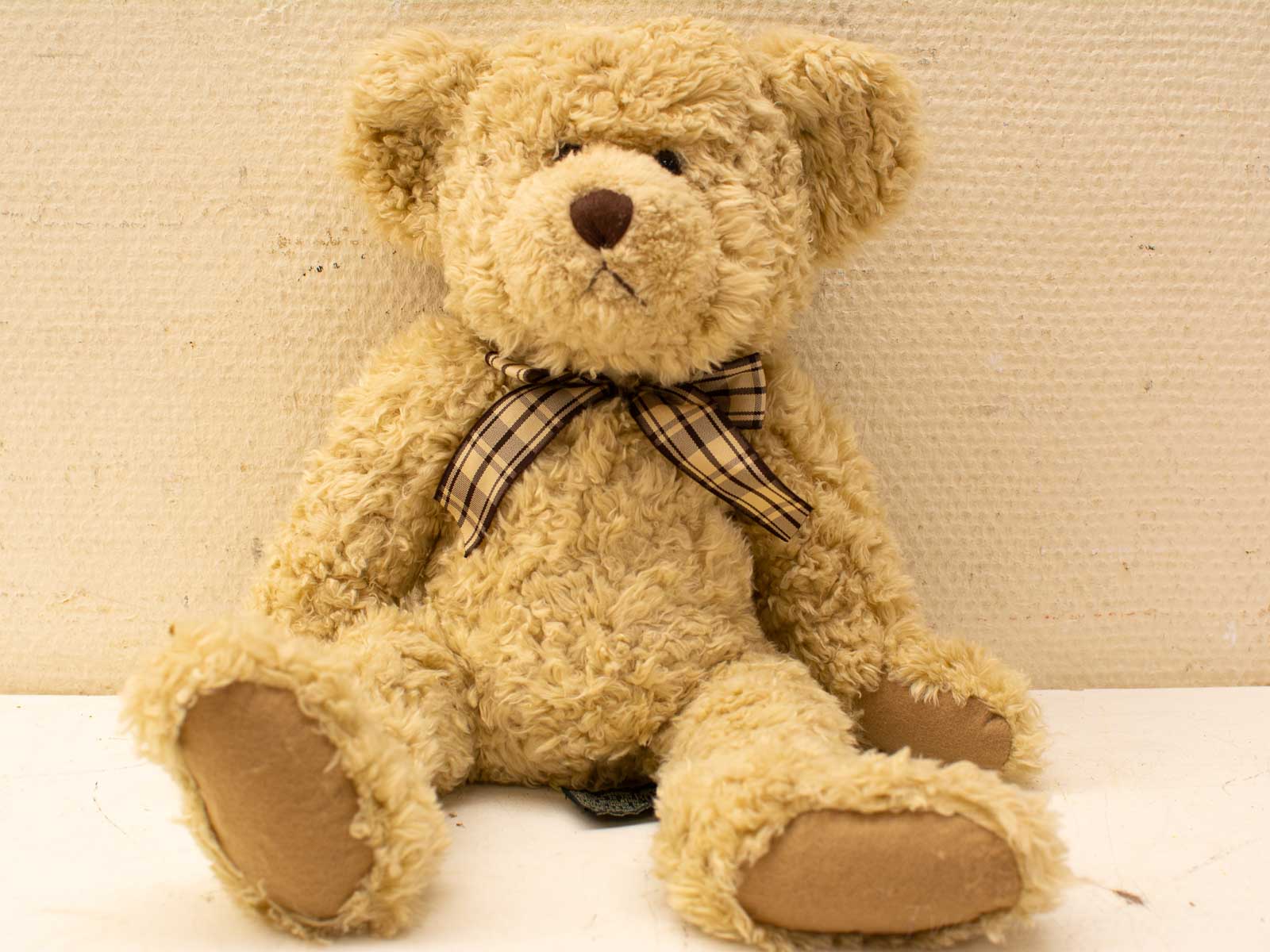 Soft beige teddy bear with plaid bow tie, perfect for comfort or vintage decor.